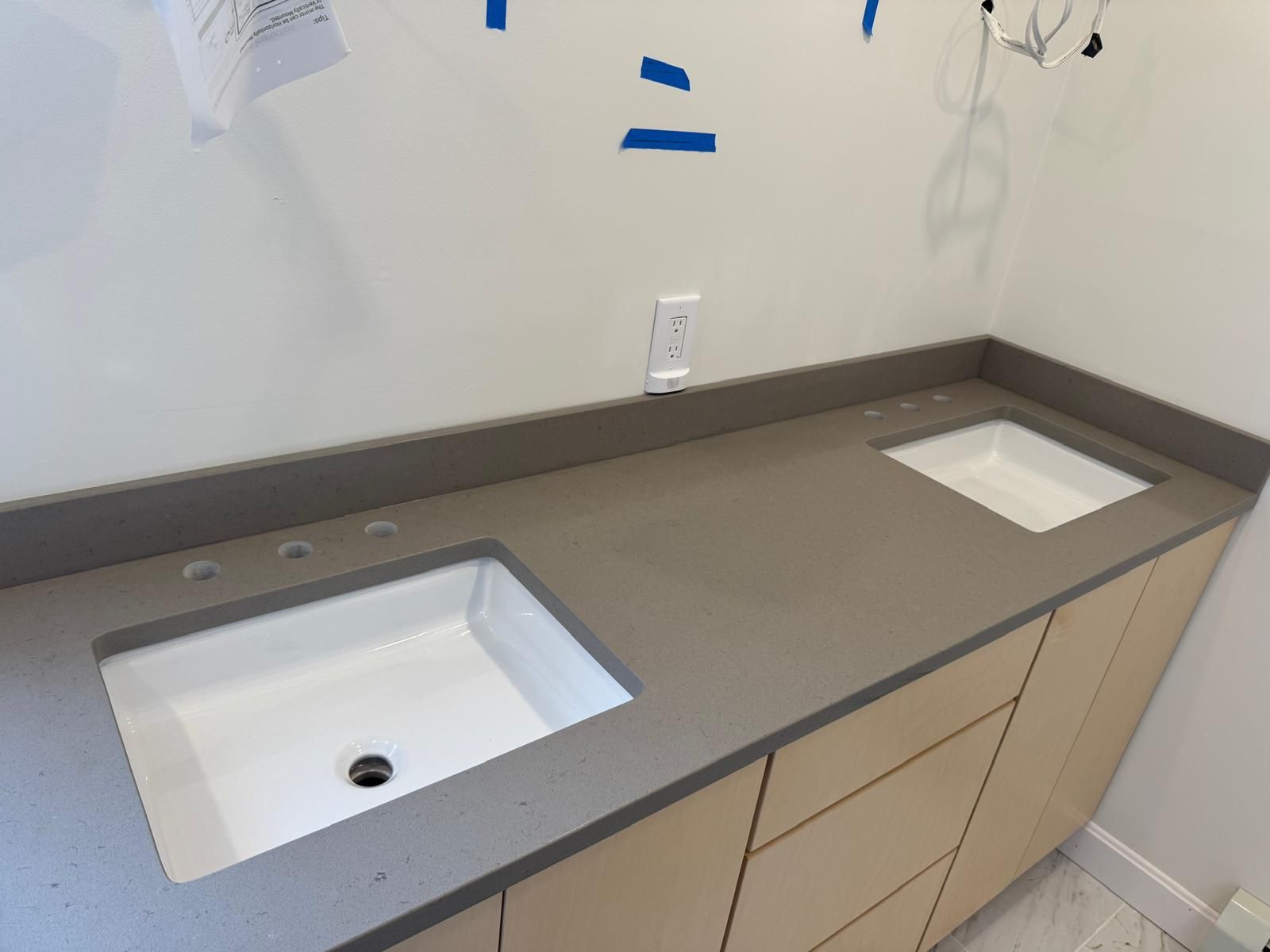 Bathroom vanity with gray countertop, two white sinks, and light wood cabinets.