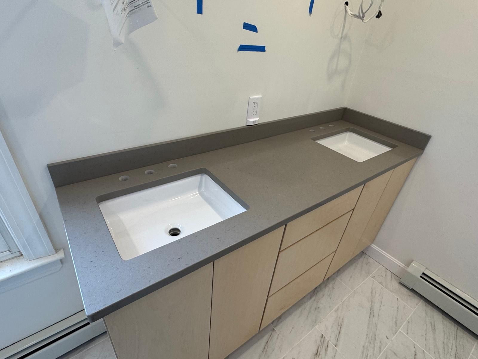 Bathroom vanity with gray countertop and two white sinks; light wood cabinets.