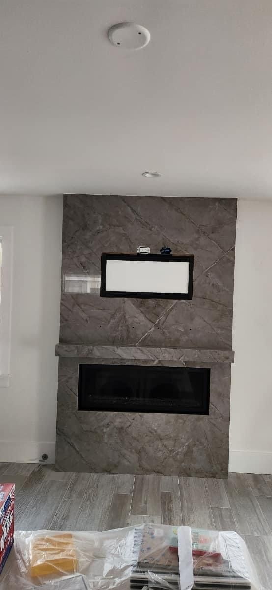 A fireplace with a gray stone facade. There is a recessed tv above the fireplace and debris on the floor.