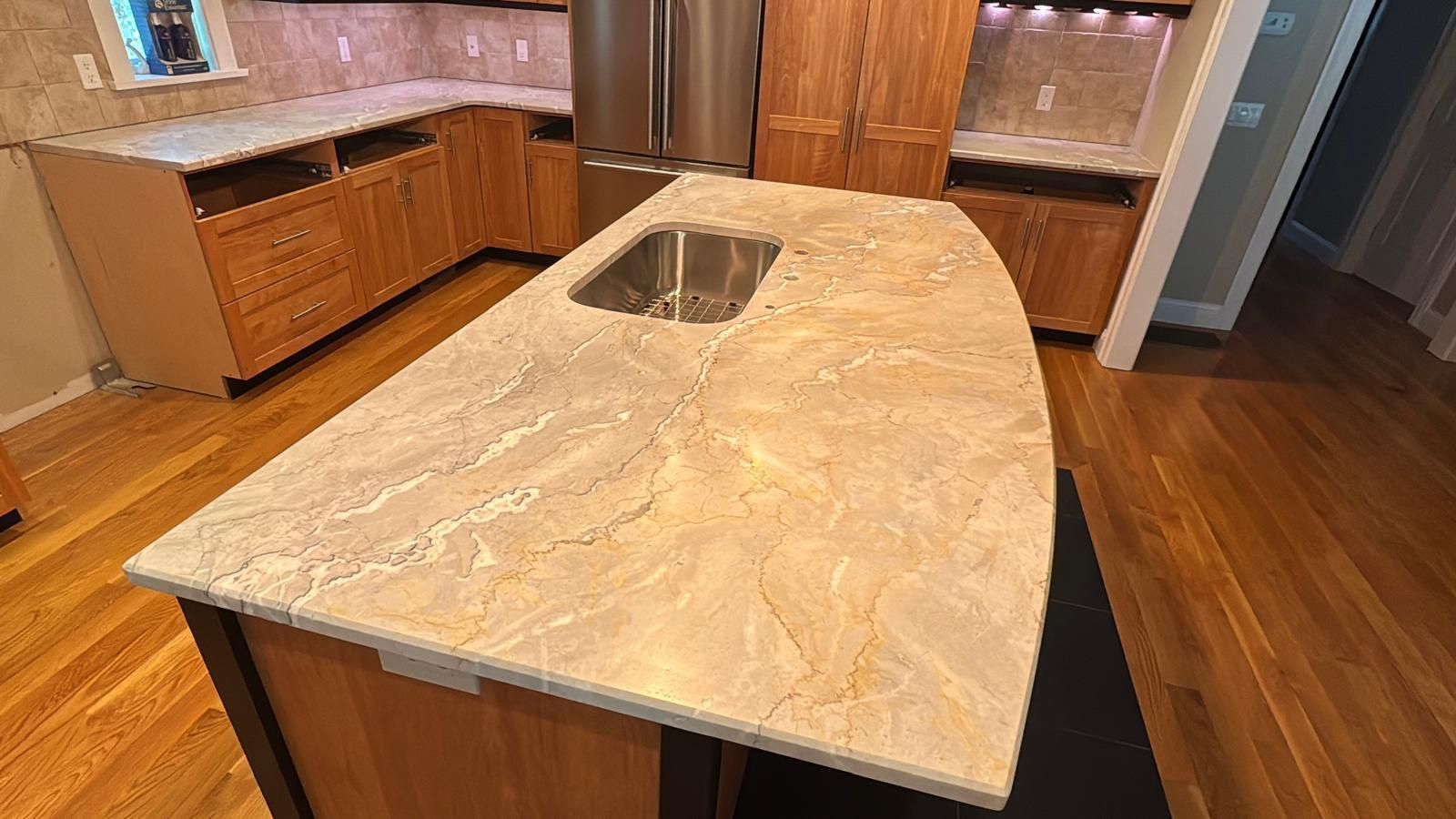 Kitchen with a light-colored granite countertop island and wooden cabinets; a stainless steel sink is in the island.