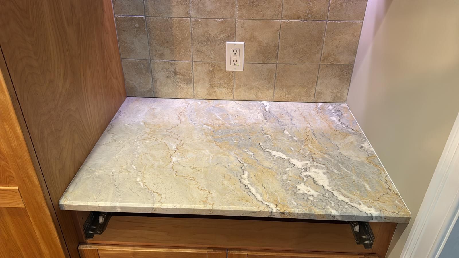 Countertop with granite surface, against tiled backsplash and cabinets, with an electrical outlet.