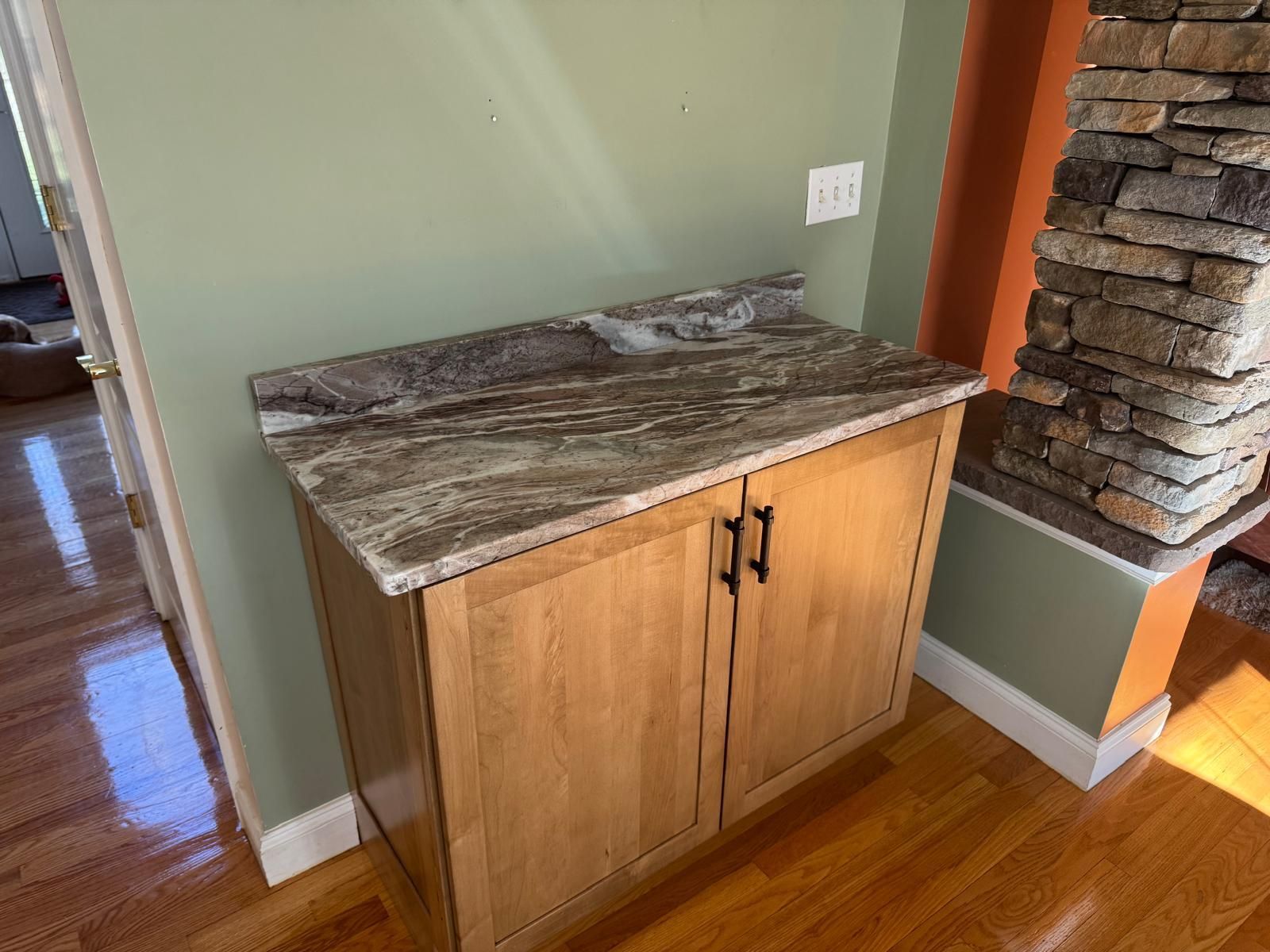 Wooden cabinet with granite countertop against a green wall, next to a stone fireplace.