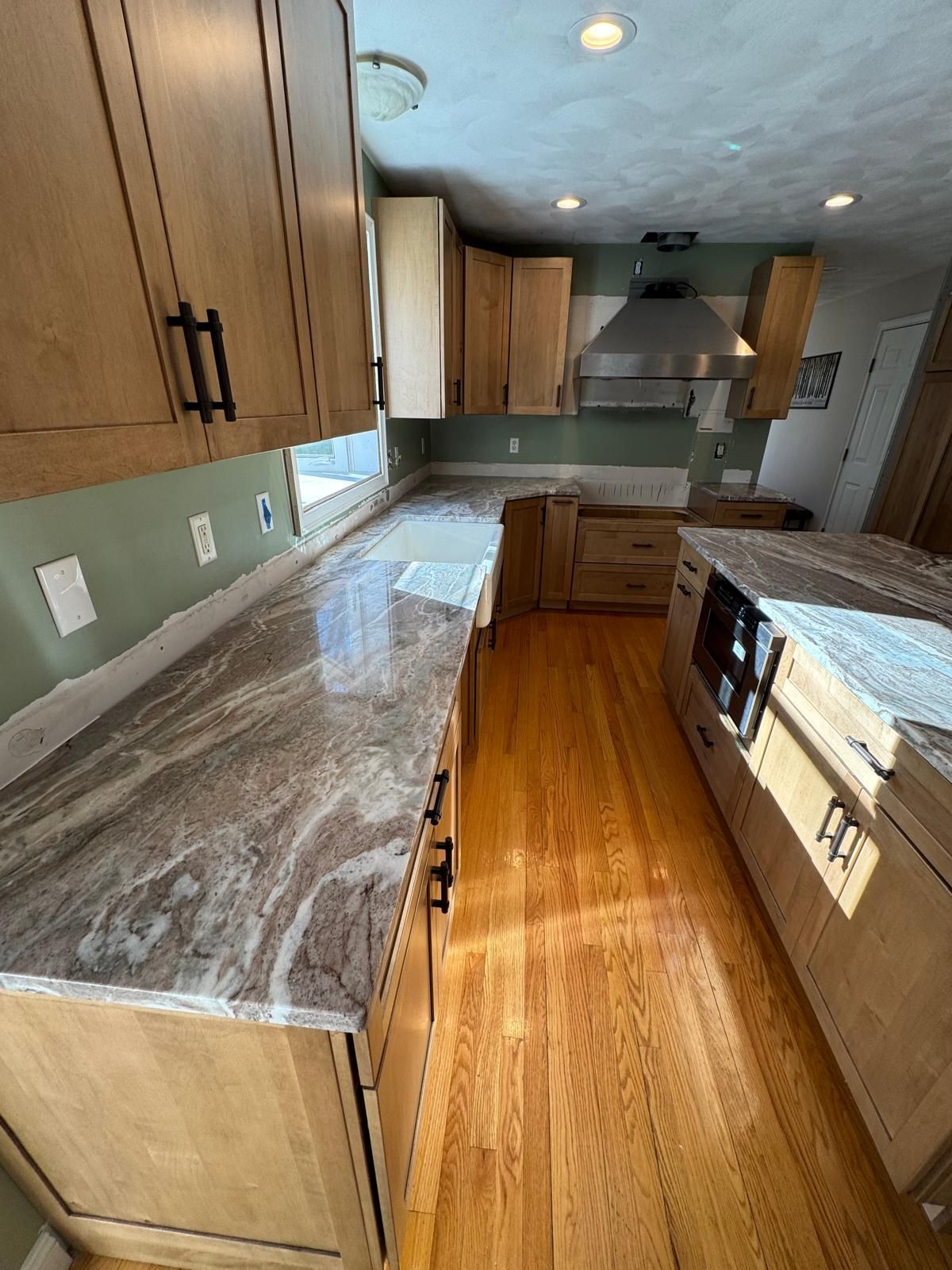 Kitchen with light wood cabinets, granite countertops, stainless steel hood, and hardwood floors.