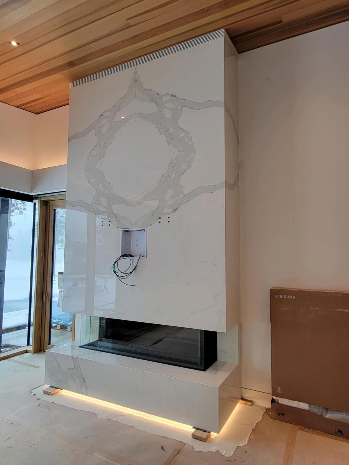 Modern white fireplace with marble-like design, built-in display, and lighting.