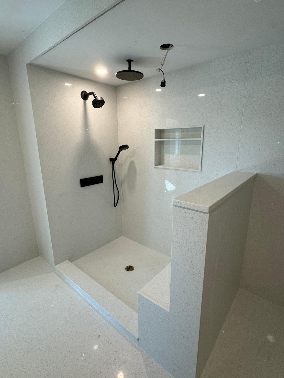 Modern white shower with black fixtures and recessed shelf.