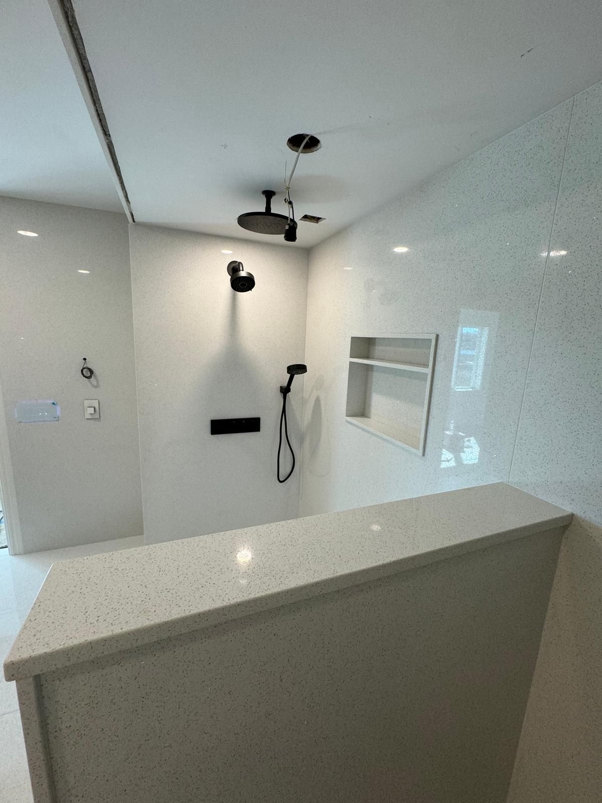 Modern white bathroom with quartz countertop, black shower fixtures, and recessed shelf.