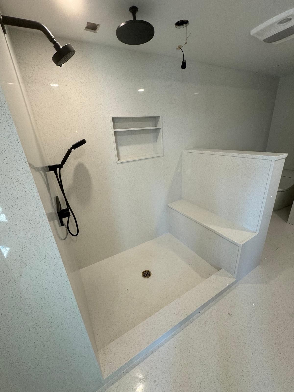 White shower with bench, multiple shower heads, and recessed shelf.