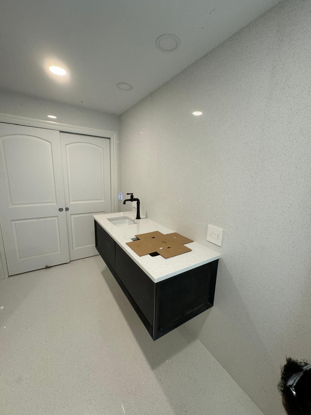 Bathroom with a floating black vanity, white countertop, and black faucet. White walls and floor, two white doors.