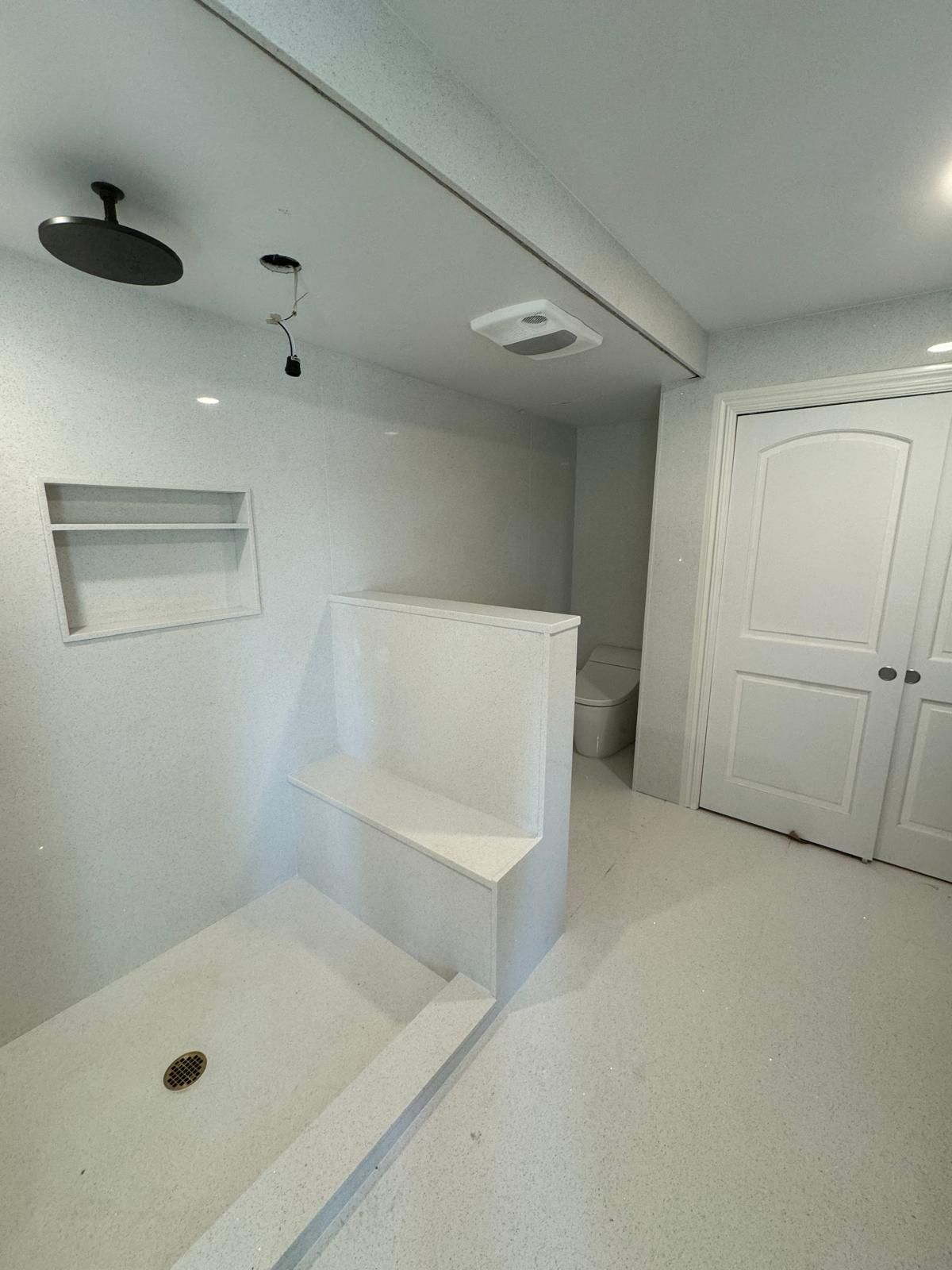 Modern white bathroom with shower bench, black showerhead, and a closed door.