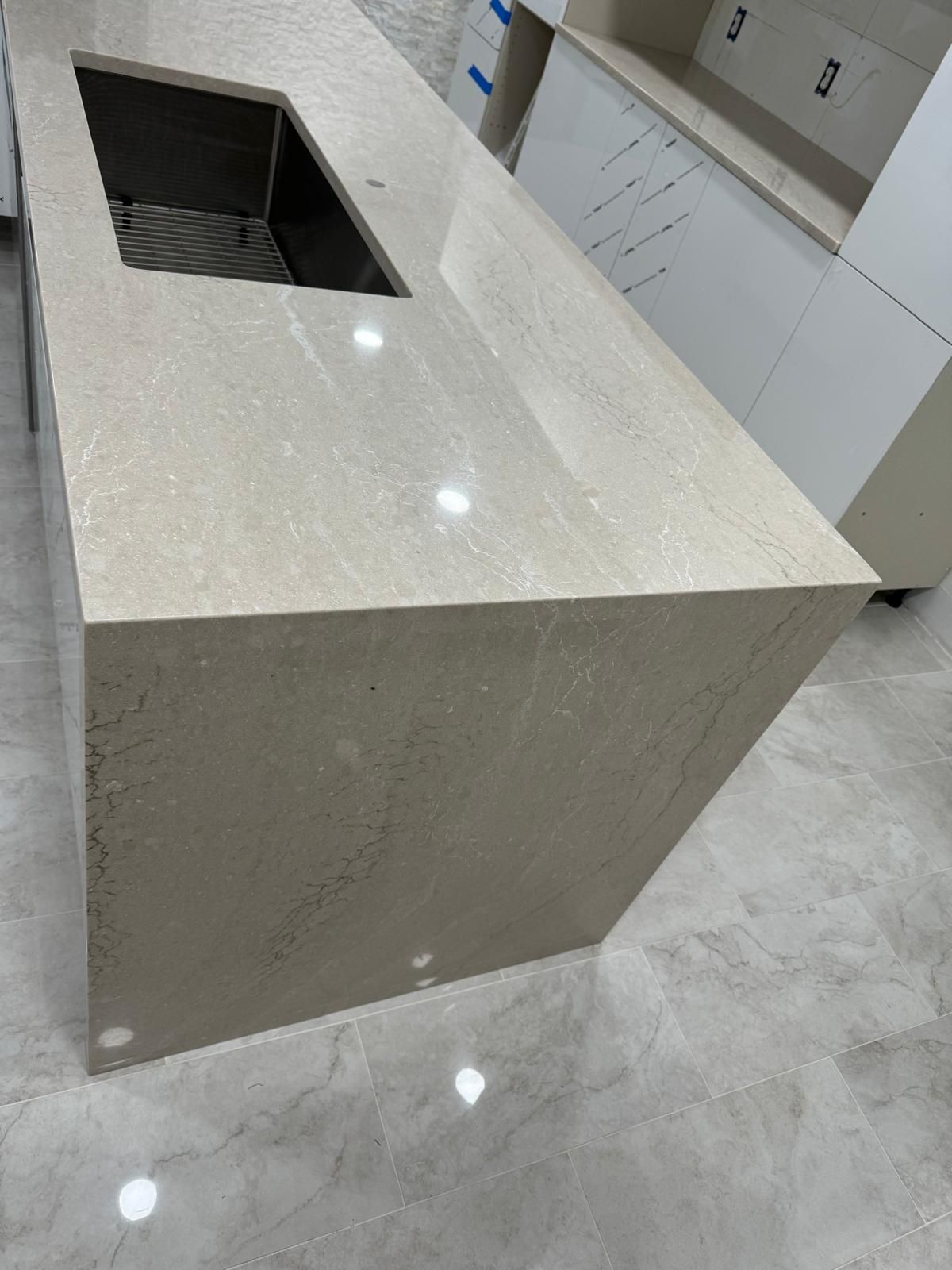 Beige quartz countertop with sink cut-out, installed on a kitchen island with white cabinets, light tile flooring.