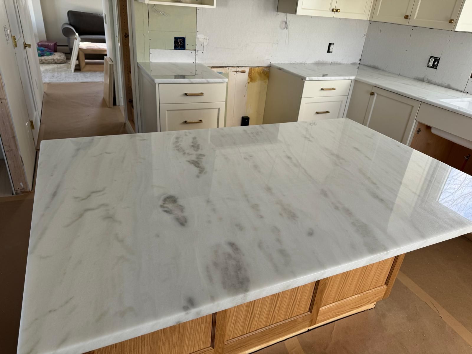 Kitchen island with white marble countertop and light wood cabinets, under construction.