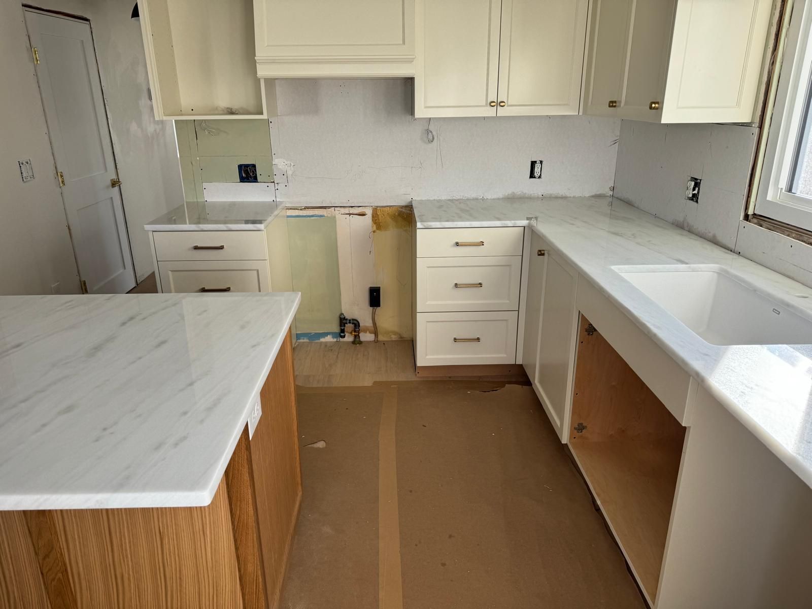 Kitchen under construction with white cabinets, countertops, and a wooden island.