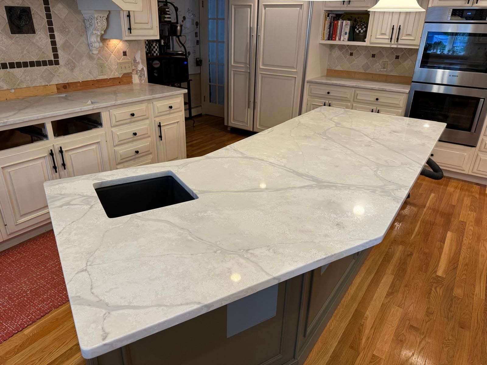 Kitchen island with white marble countertop, black sink, and light wood cabinets.