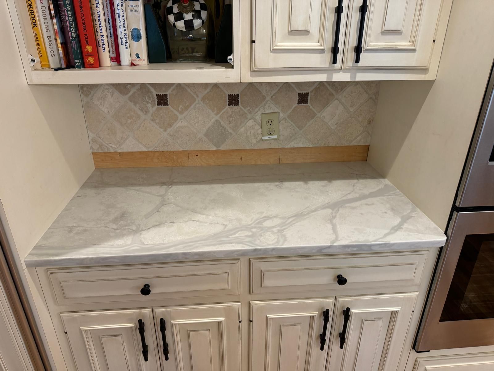 Kitchen cabinet with marble countertop, backsplash, and cookbooks on the shelf.