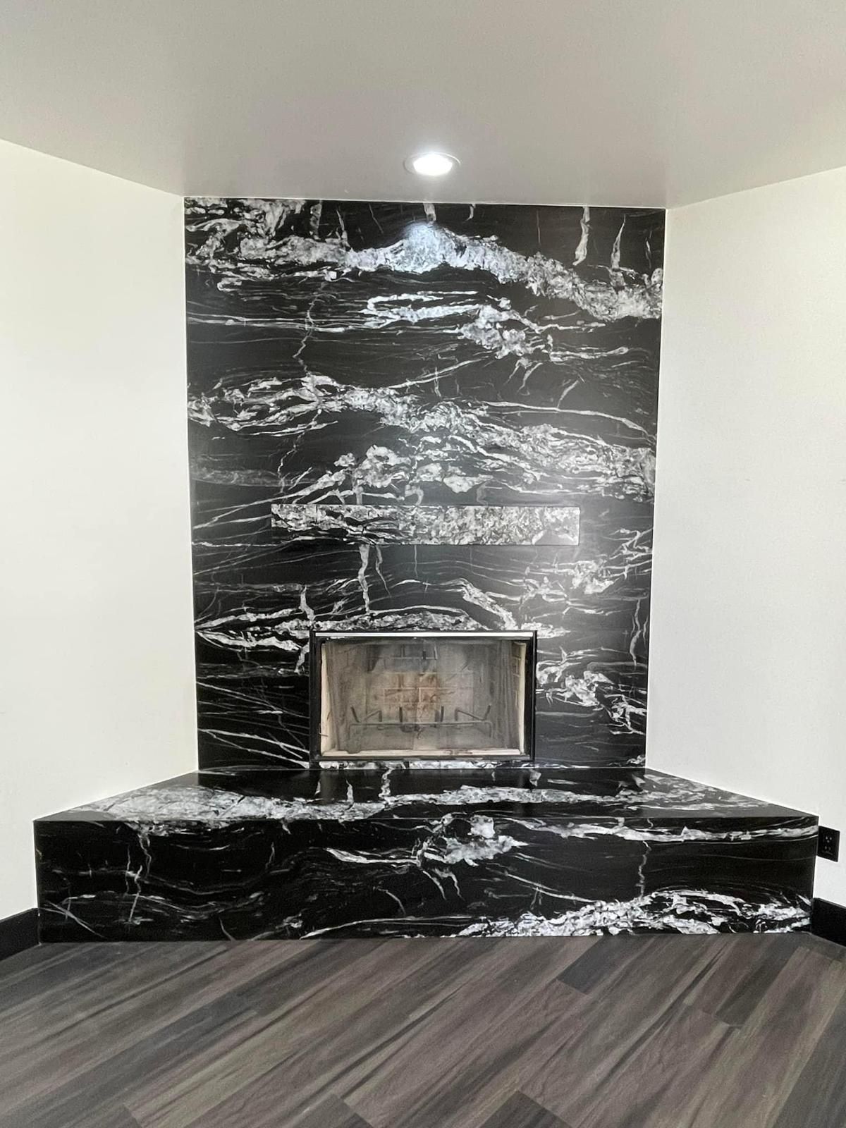 Black and white marble fireplace with a hearth, set in a corner of a room with dark wood flooring.