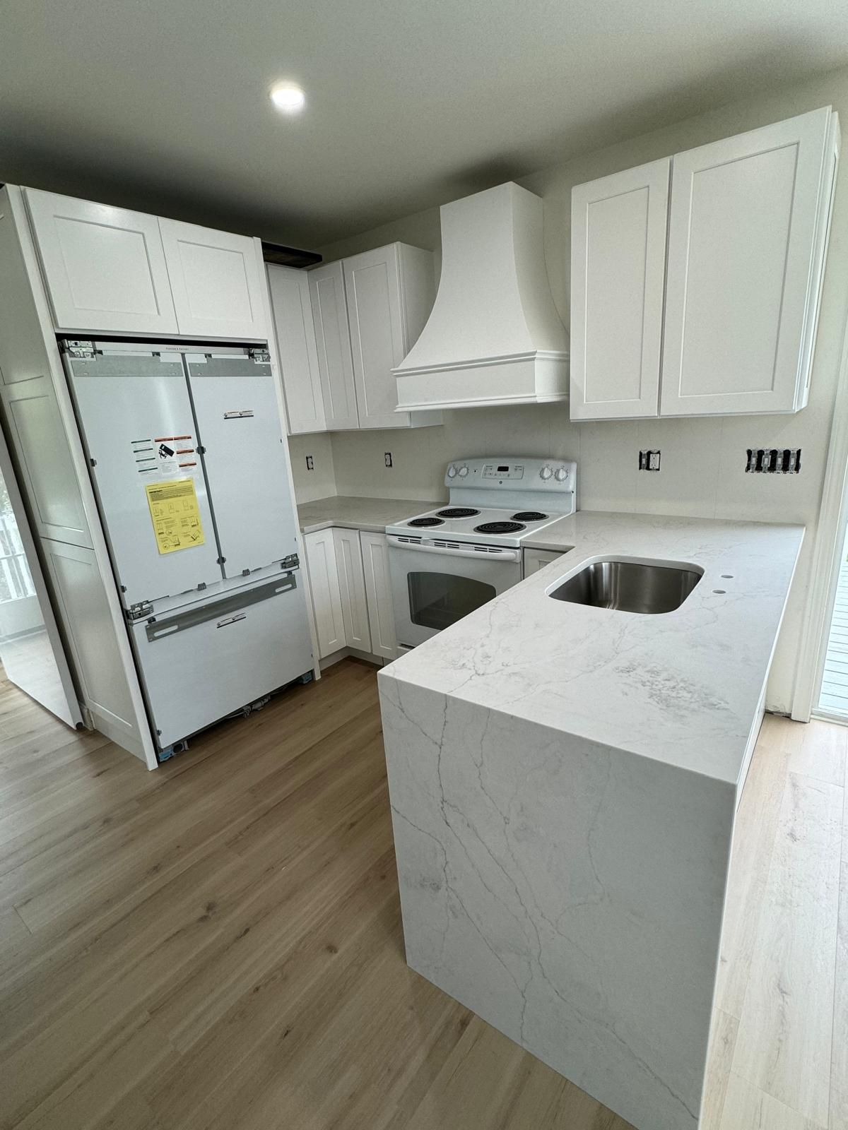 Modern white kitchen with island, range, and refrigerator. Light wood-look flooring.