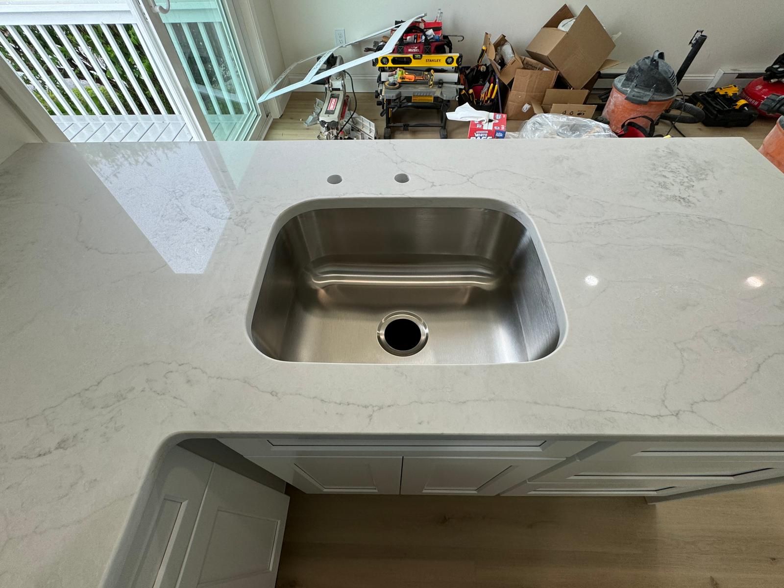 Stainless steel kitchen sink installed in white countertop.