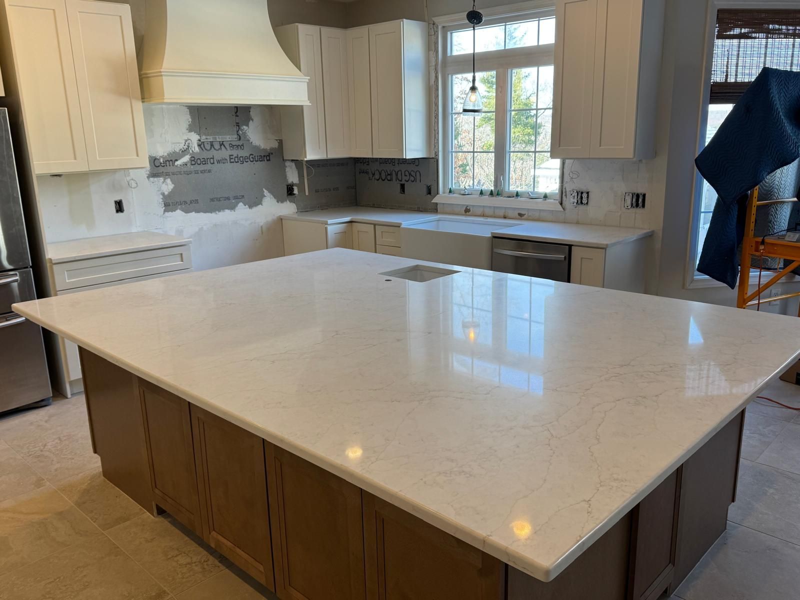Kitchen with large island, white countertops, brown cabinets, and partially installed cabinets, and window.