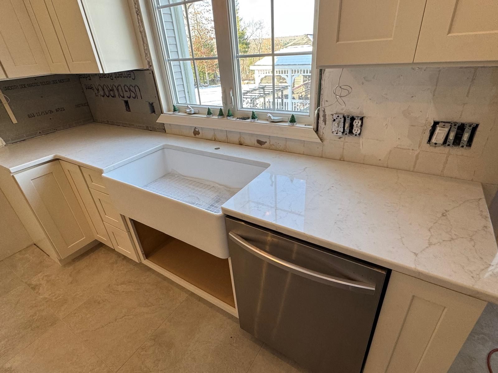 Kitchen with white countertops, sink, cabinets, and a stainless steel dishwasher near a window.