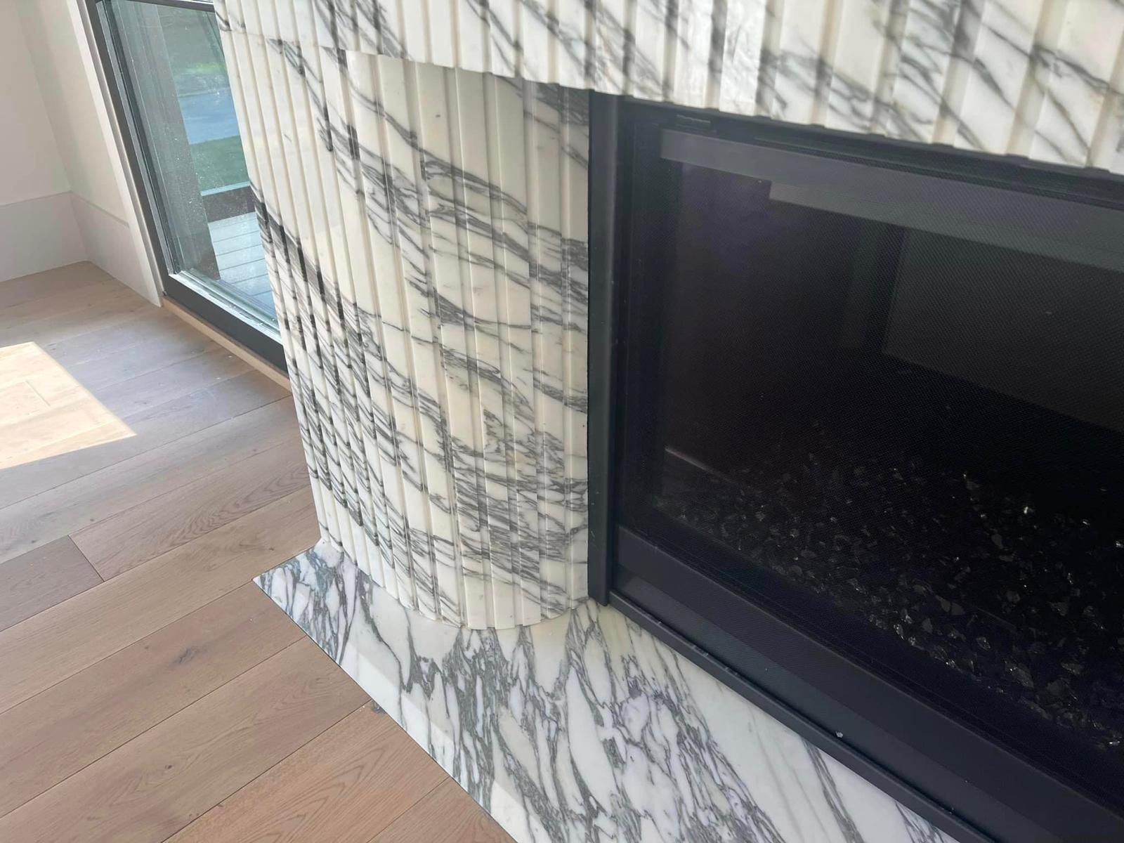 Close-up of marble fireplace with black framed opening, and light wooden floor.