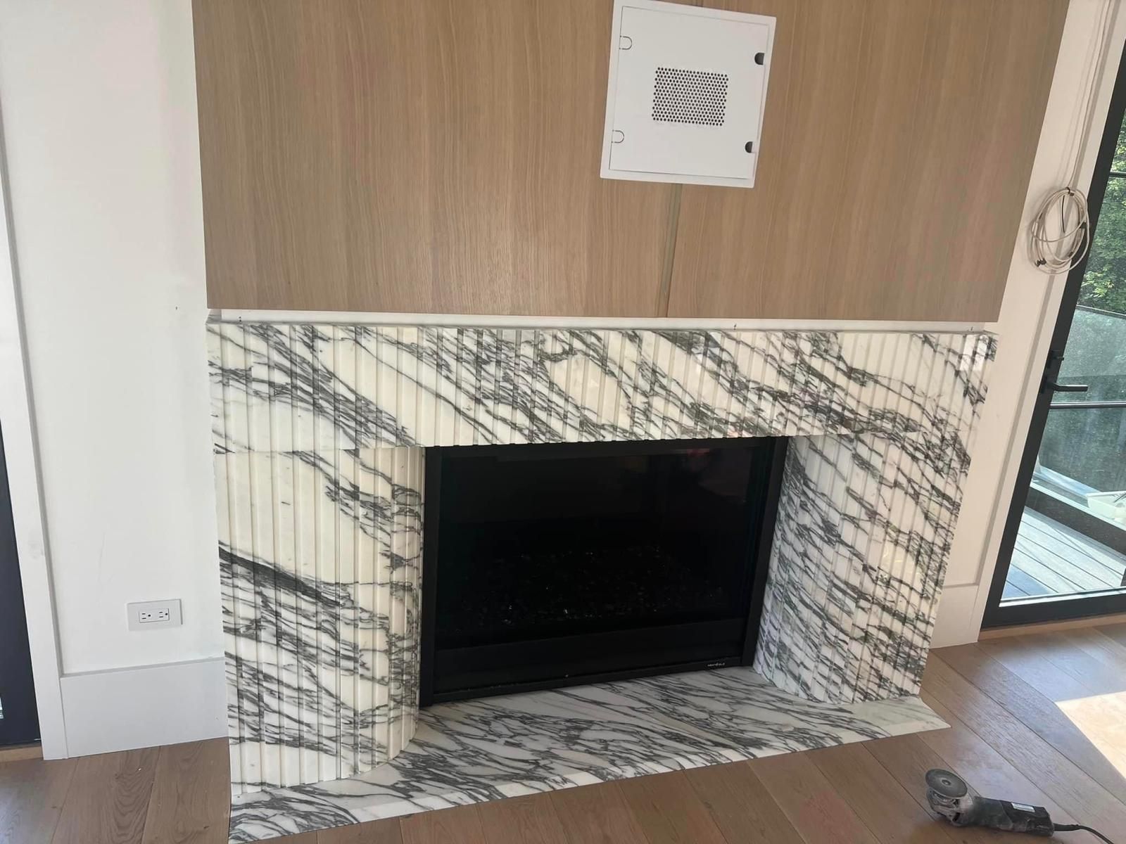 Marble fireplace with a black rectangular opening, set against light wood paneling.