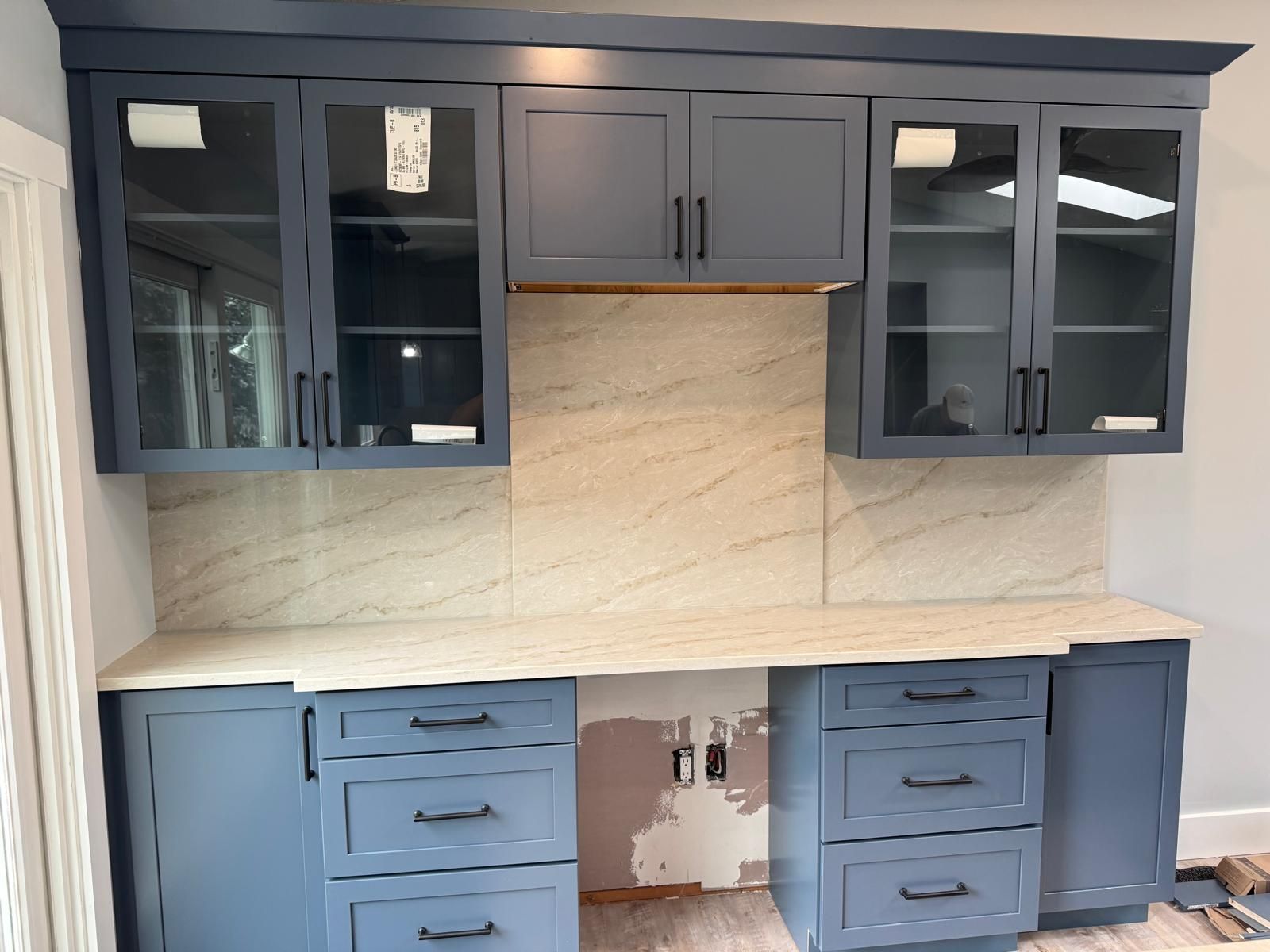 Blue kitchen cabinets with glass doors, granite backsplash, and countertop, with open space below.