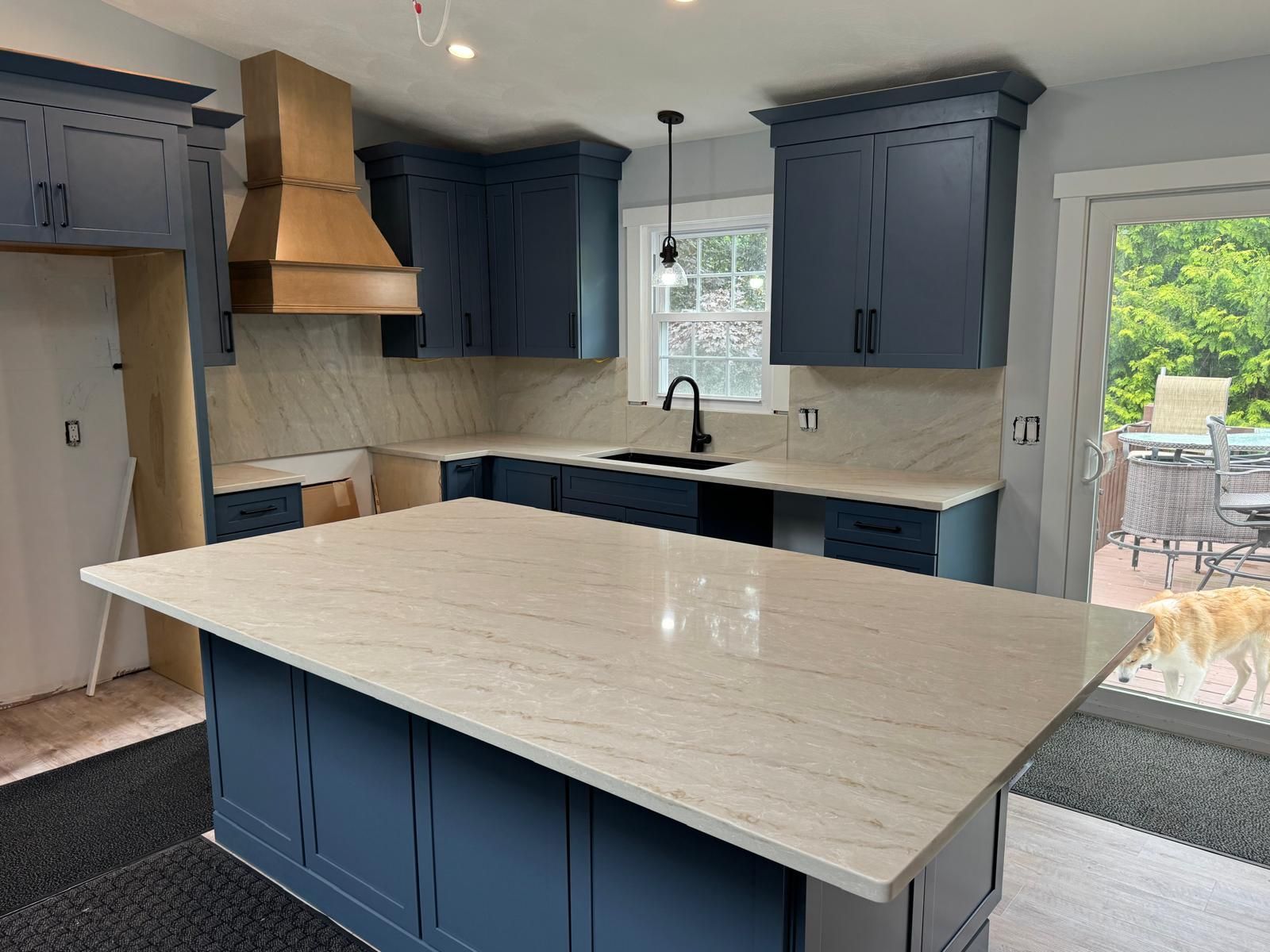 Blue kitchen with light countertops, wooden range hood, and island.