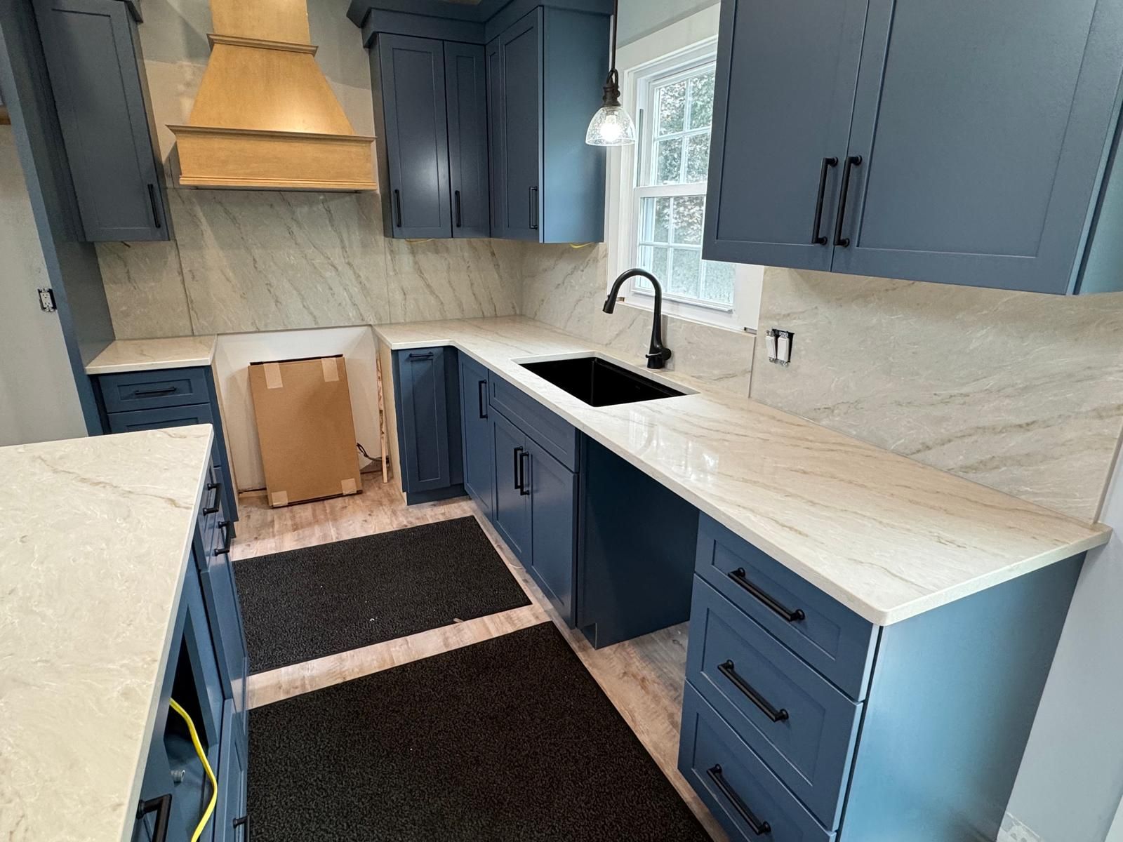 Blue kitchen with wood range hood, light countertops, black sink, and hardware.