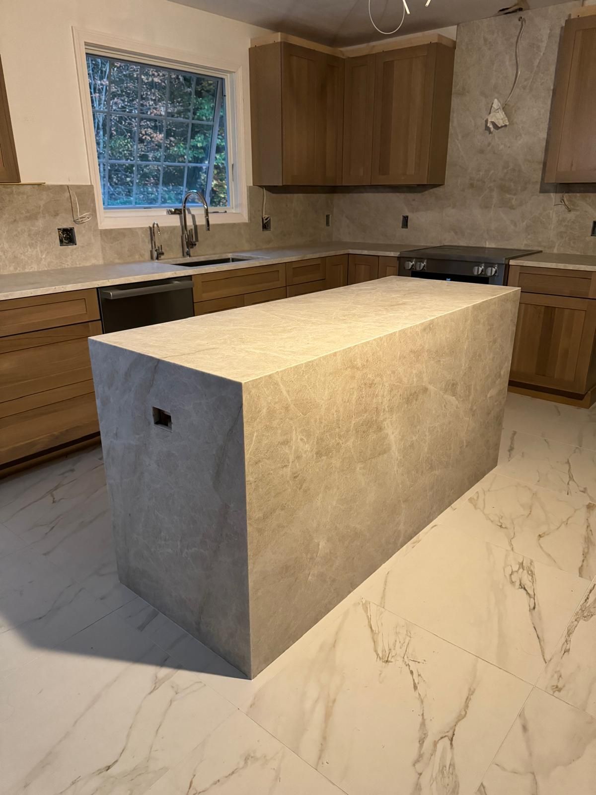 Kitchen renovation: light wood cabinets, stone island, marble floors, window, and appliances.