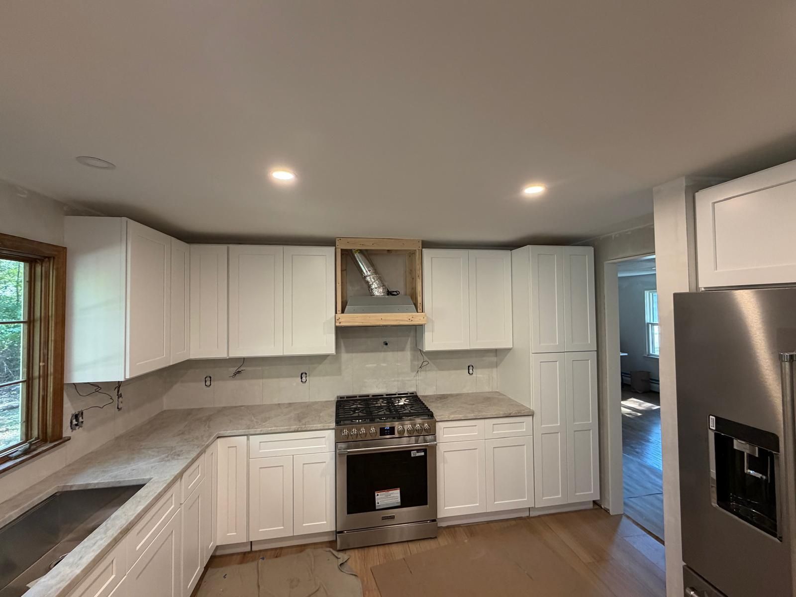 White kitchen with cabinets, stove, and a range hood under construction.