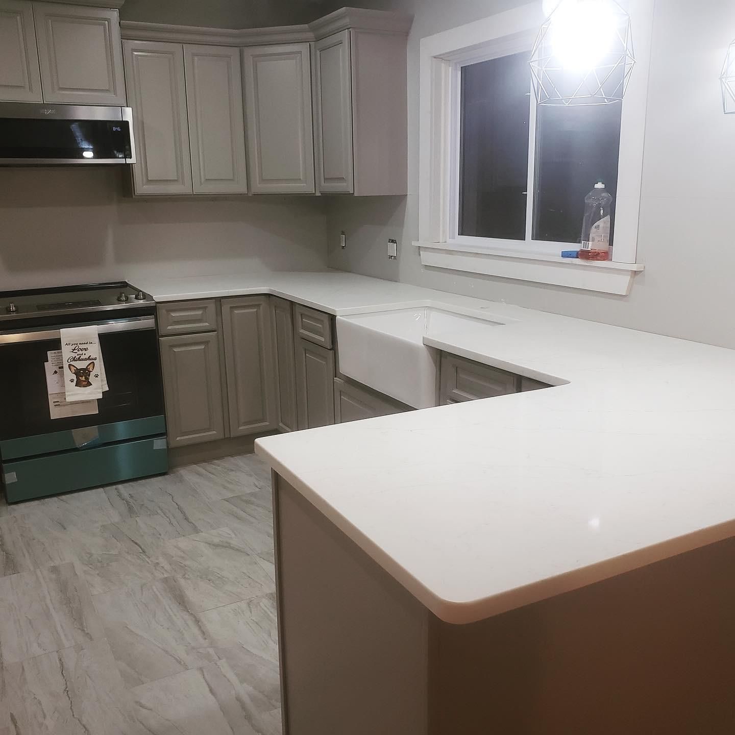 Gray kitchen with white countertops and cabinets. Includes a stove, sink, and window.