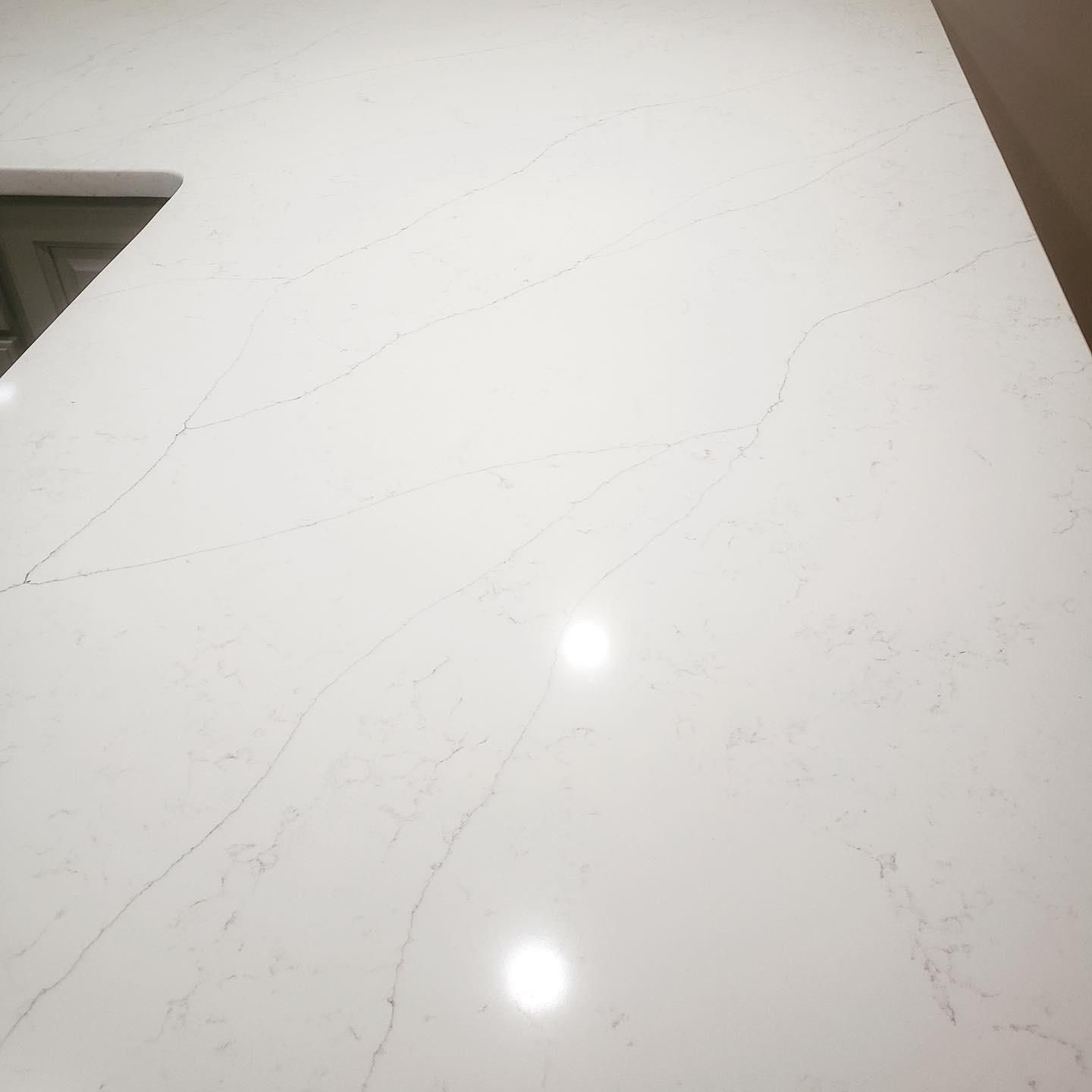 White countertop with light gray veining, lit by two bright reflections.