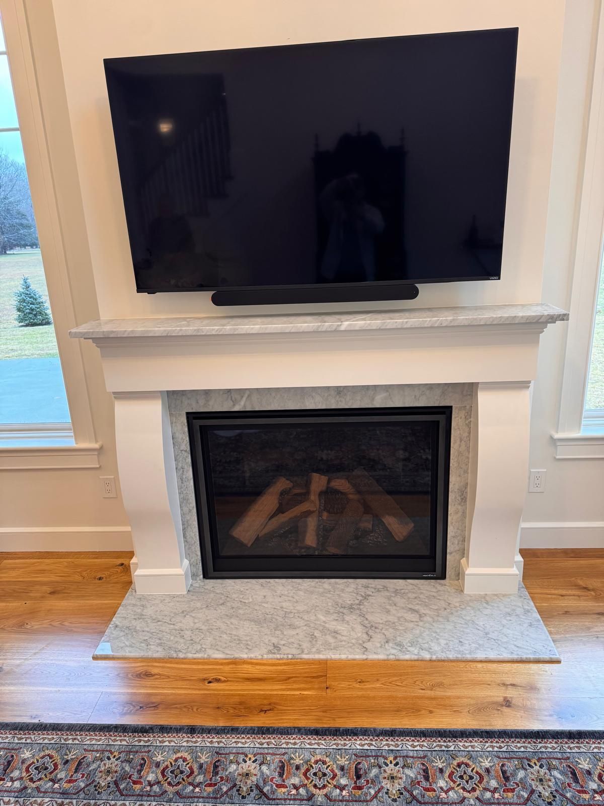 Fireplace with mounted TV and soundbar. White mantel, gray granite hearth, wooden floor.