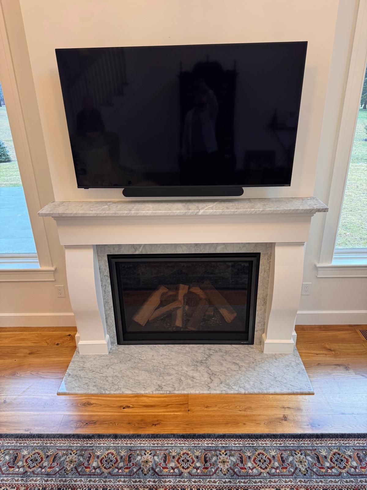 Fireplace with marble surround, TV above, and soundbar below the TV. Wooden floor with a rug.