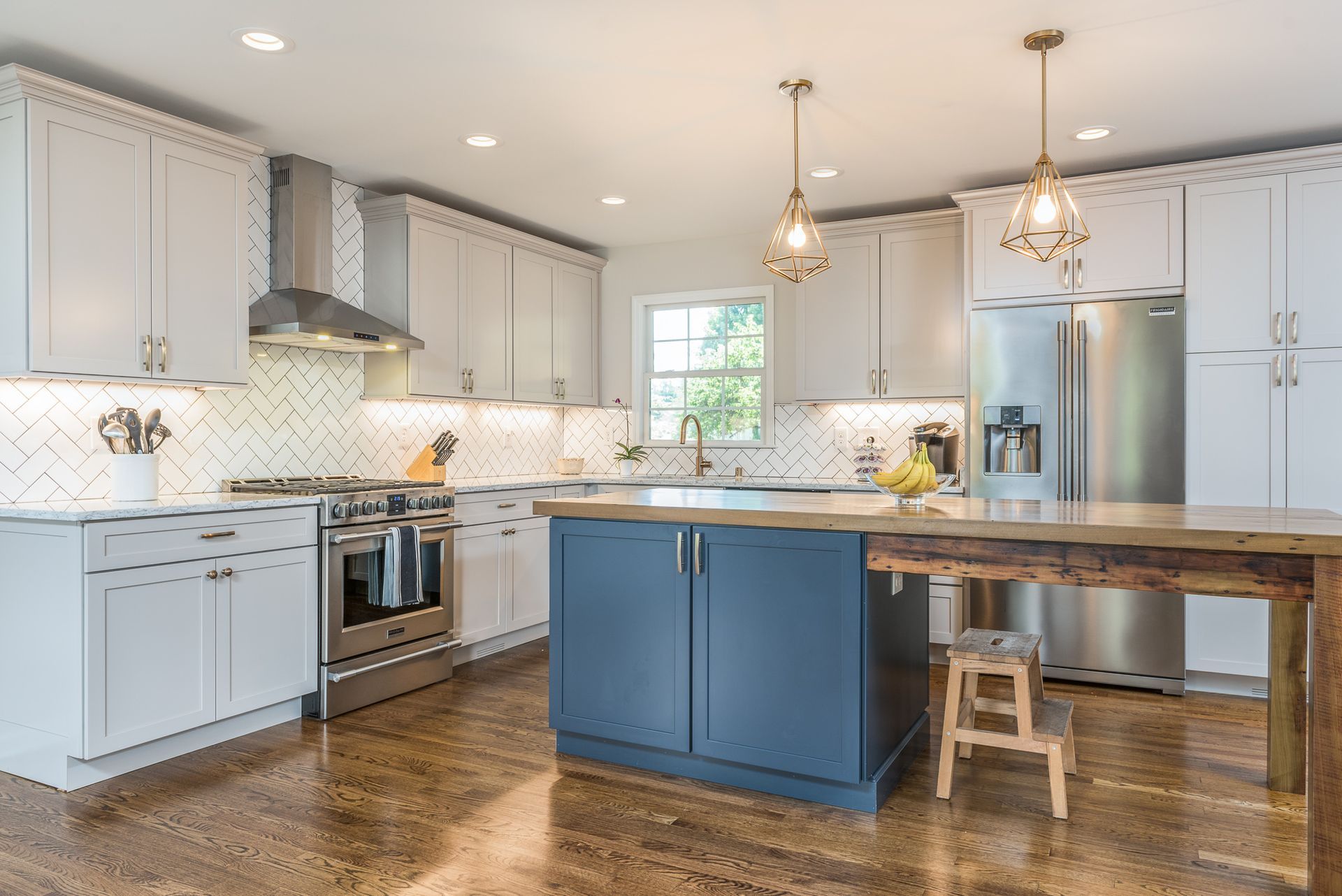 A kitchen with white cabinets , stainless steel appliances , a large island and a wooden table.