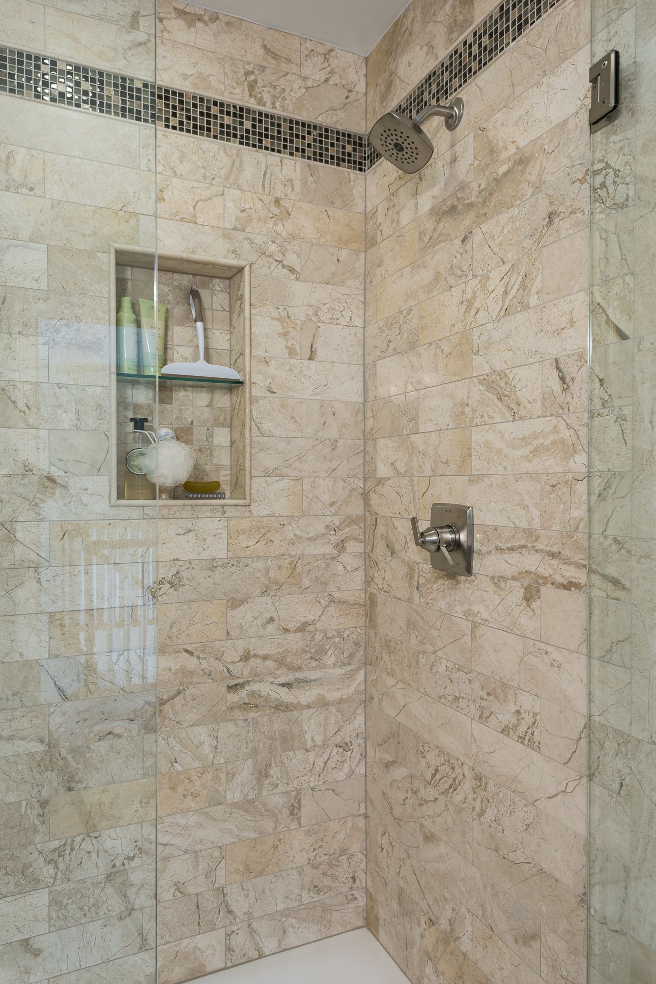 A bathroom with a walk in shower with a glass door and a shelf.