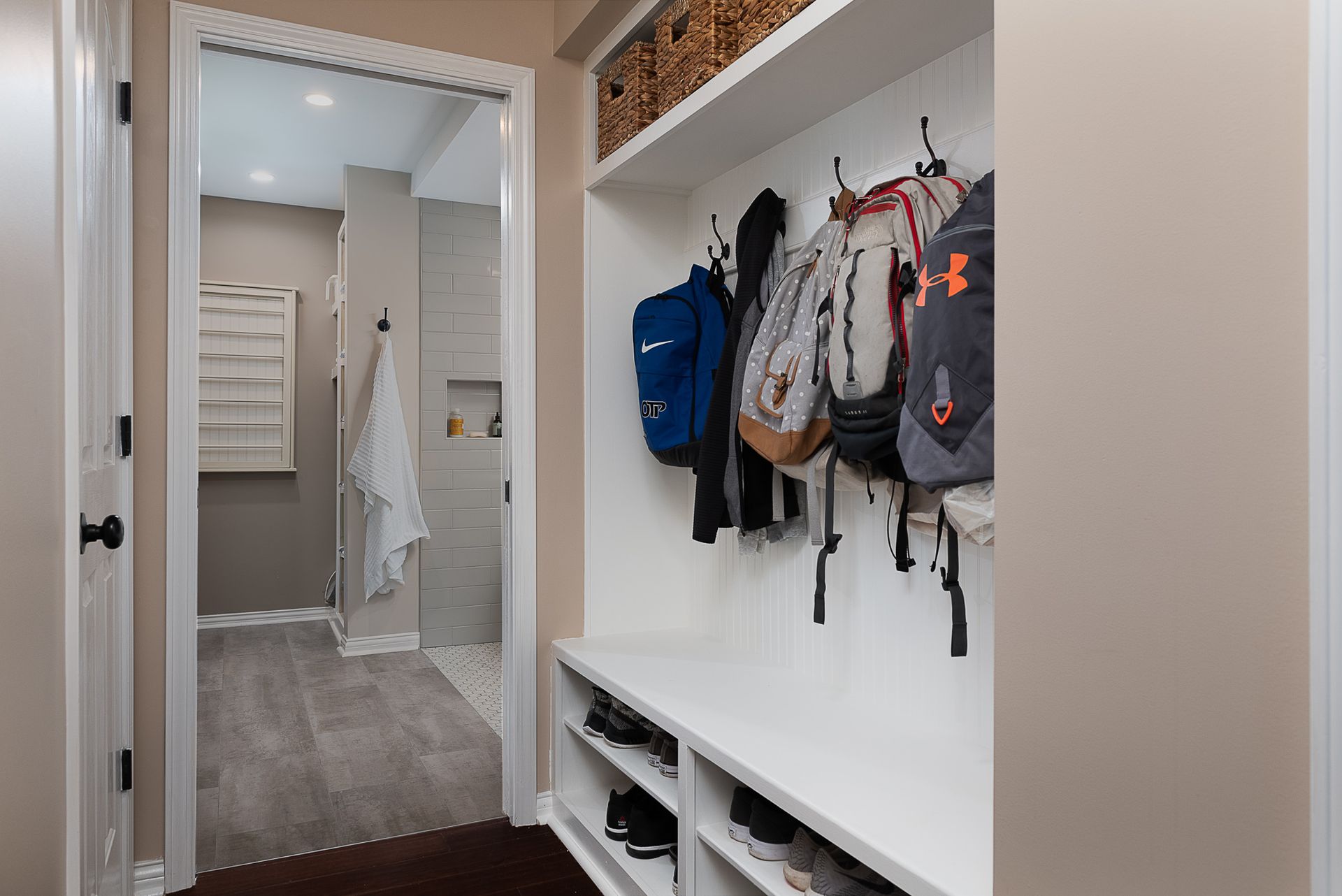 A hallway with backpacks hanging on the wall and a shoe rack.