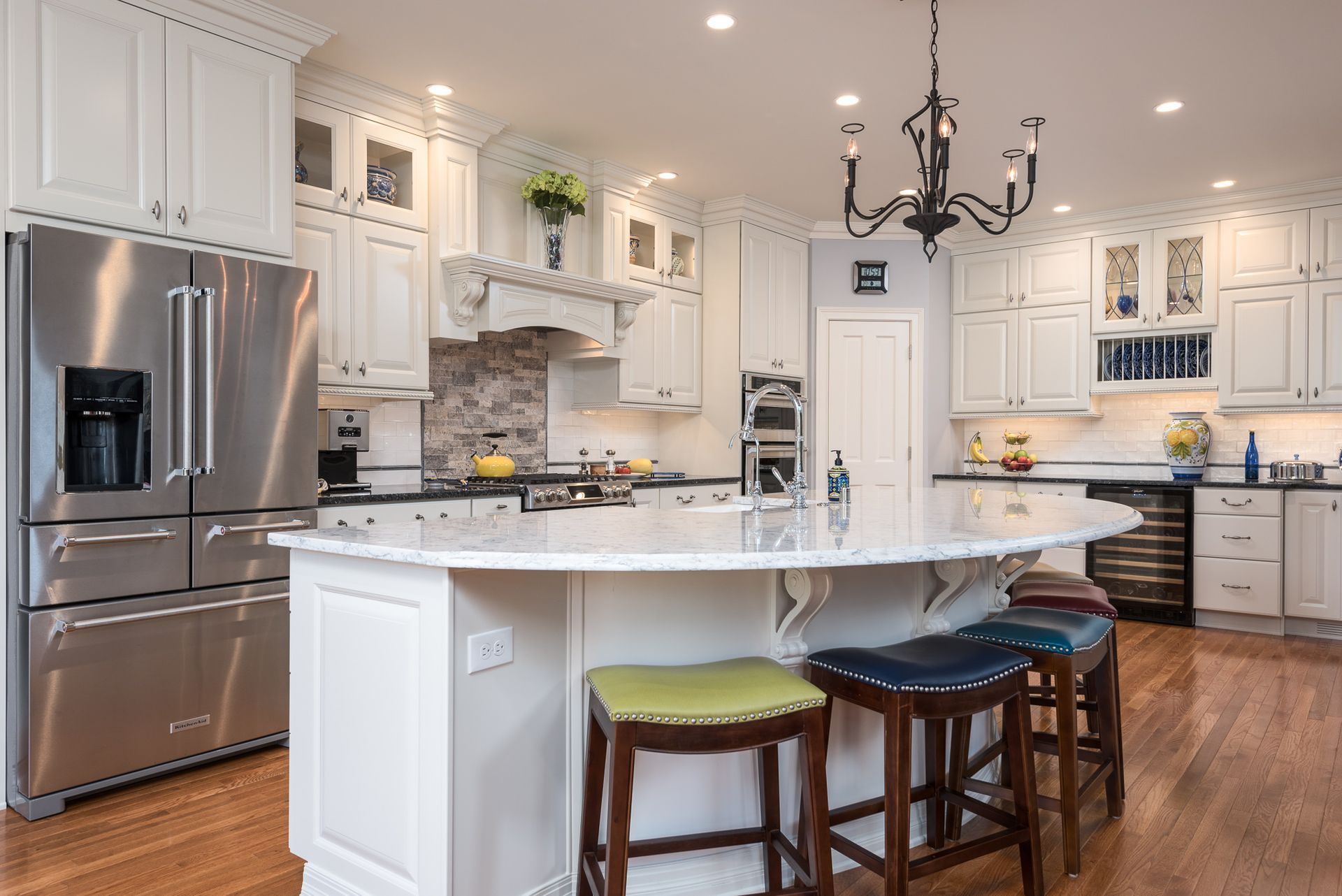 A kitchen with white cabinets , stainless steel appliances , a large island and a chandelier.
