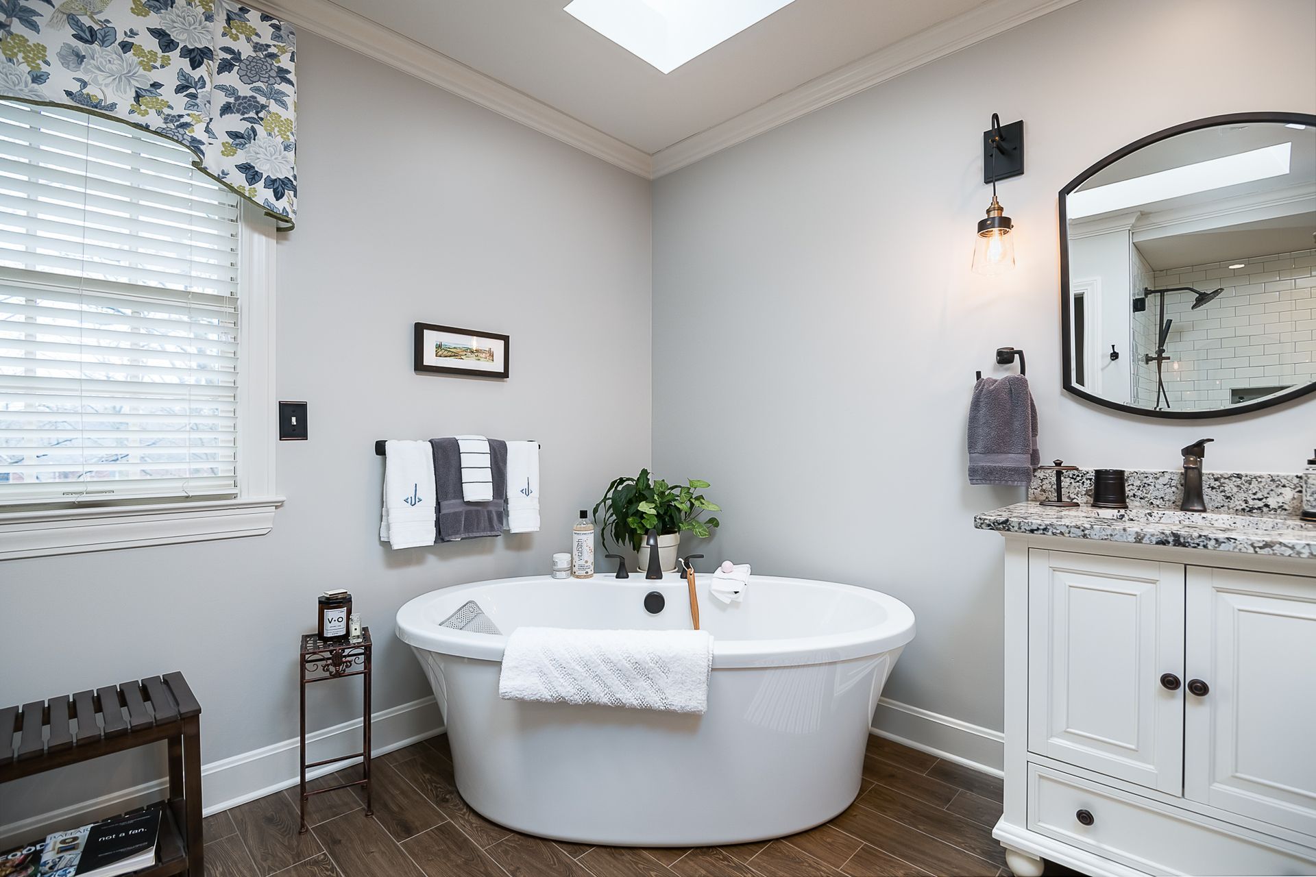 A bathroom with a tub , sink , mirror and window.