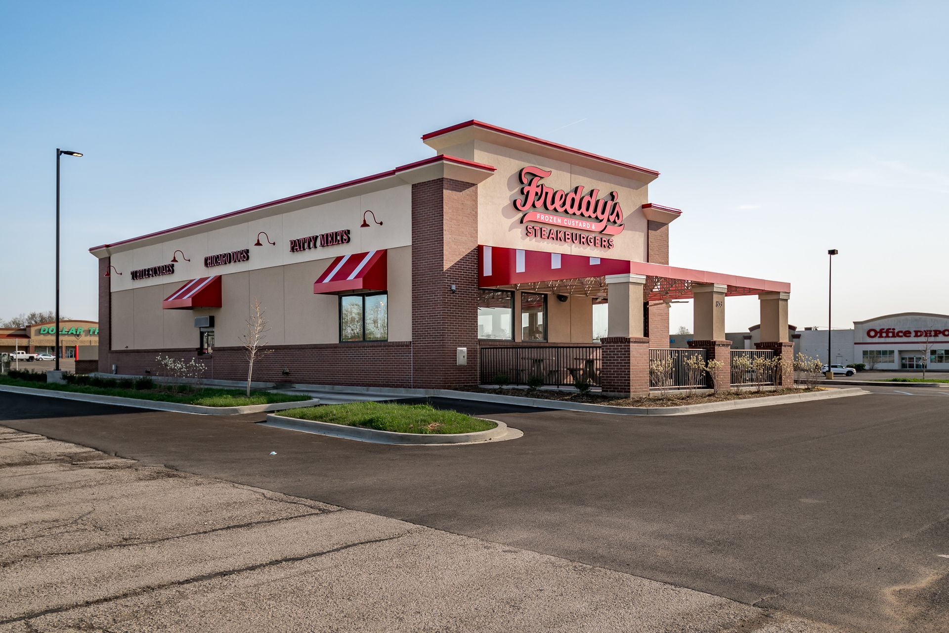 A fast food restaurant with red awnings and a parking lot in front of it.