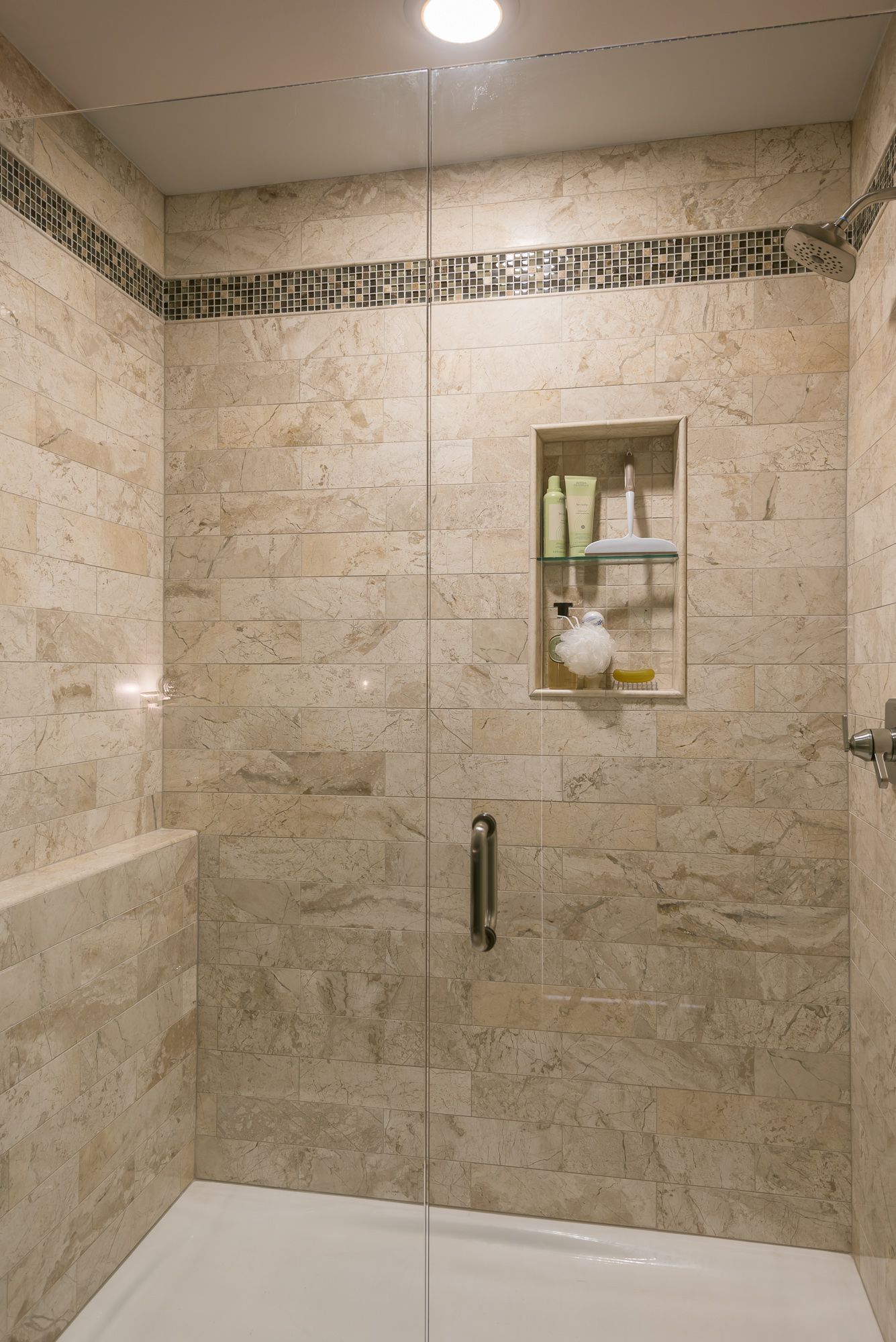 A bathroom with a walk in shower with a glass door and a shelf.
