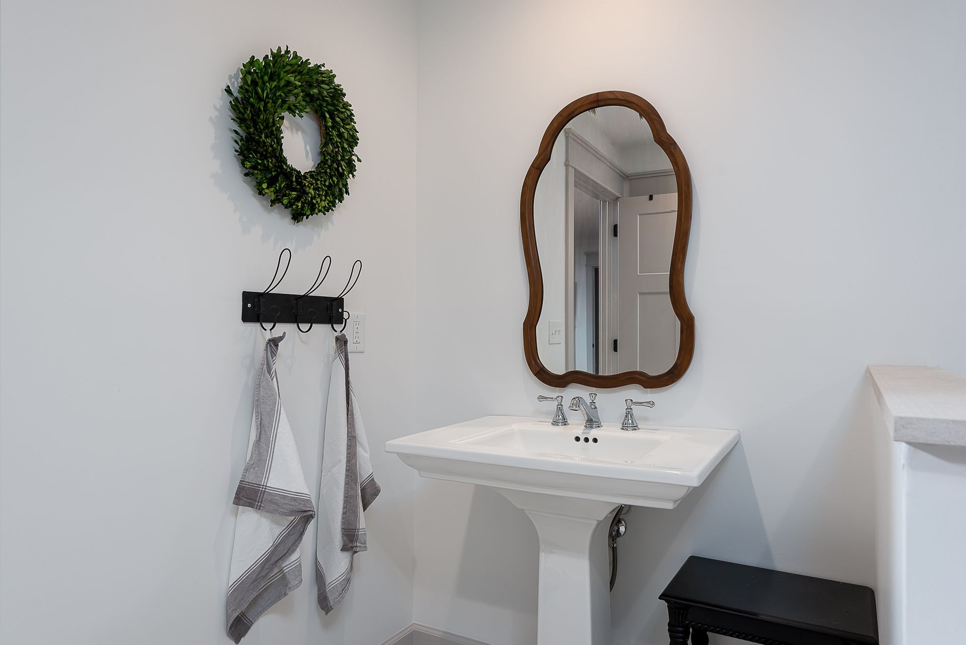 A bathroom with a sink , mirror and wreath on the wall.