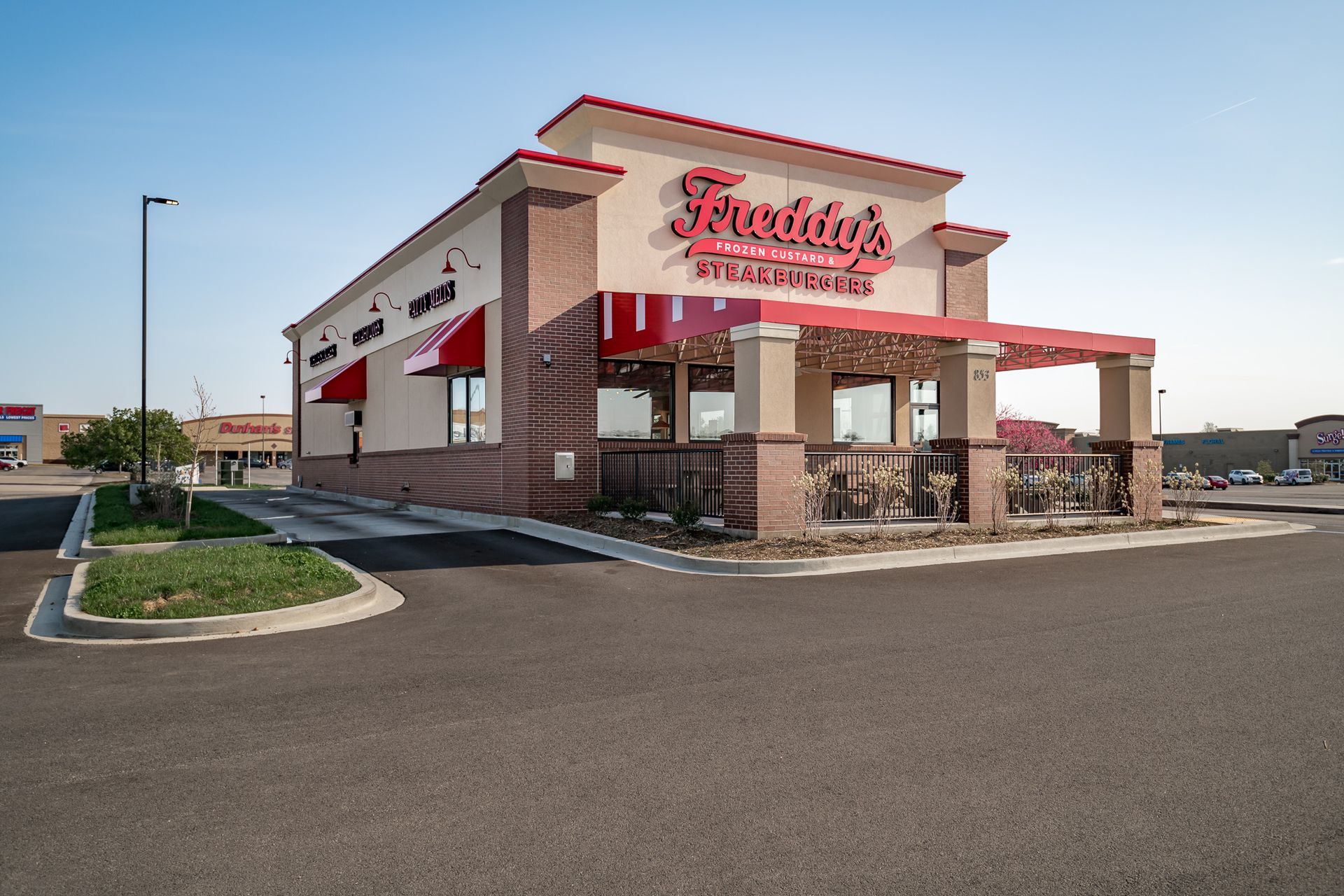 A fast food restaurant with a red awning is located in a parking lot.