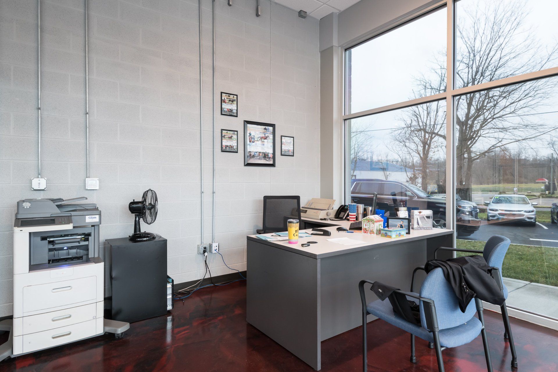 A room with a desk , chairs , a printer and a fan.
