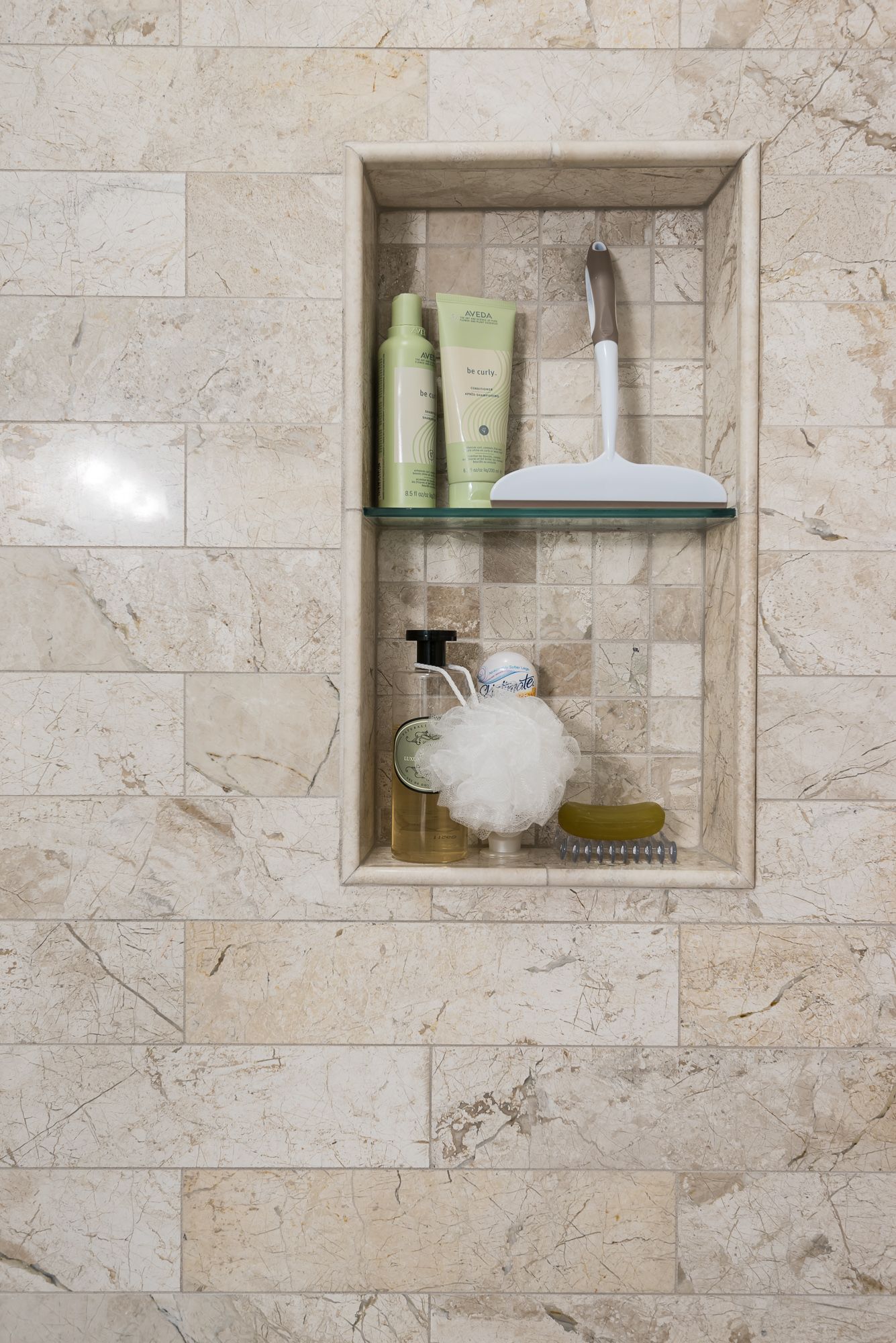There is a shelf in the shower with bottles of shampoo and a sponge.