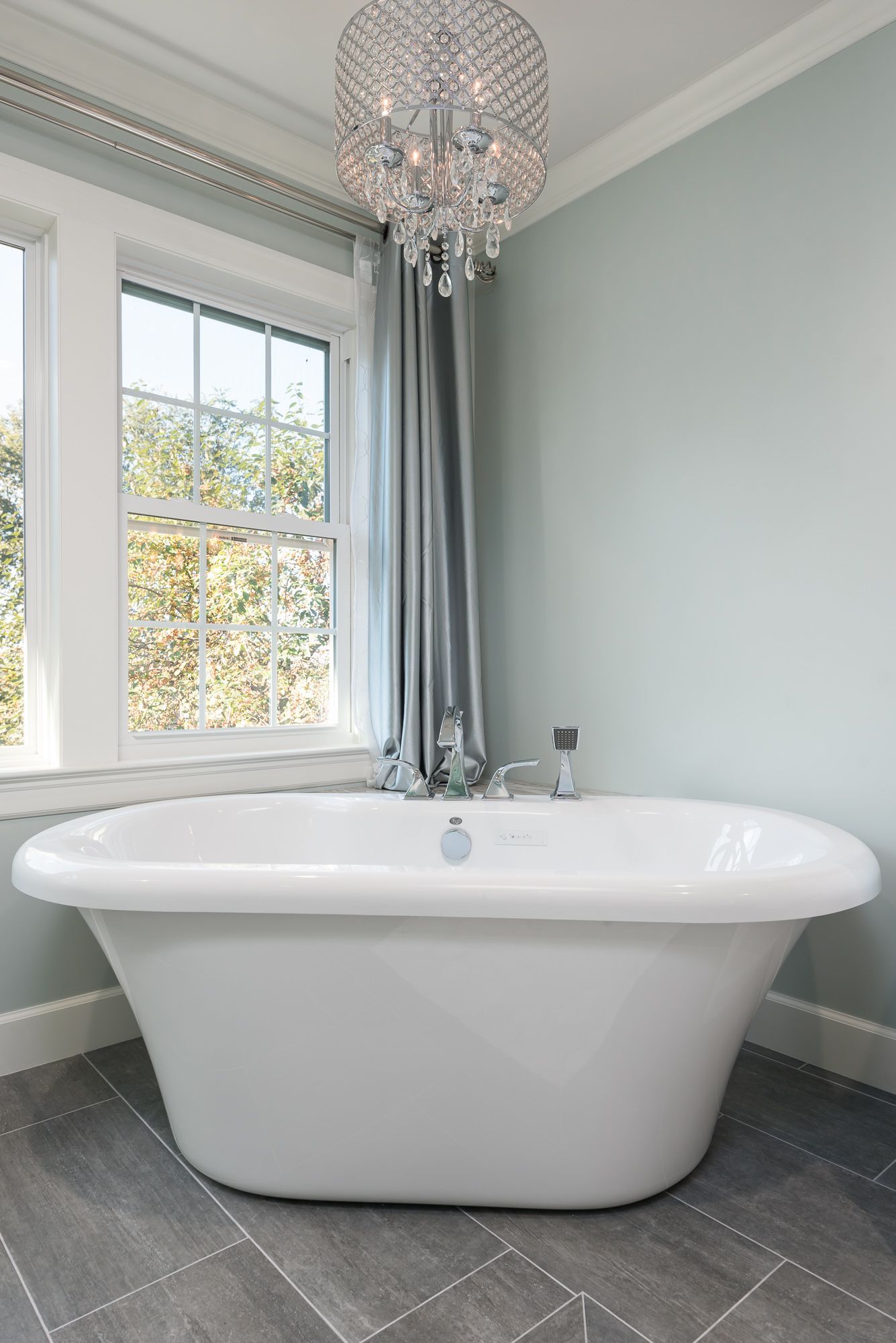 There is a bathtub in the bathroom with a chandelier hanging from the ceiling.