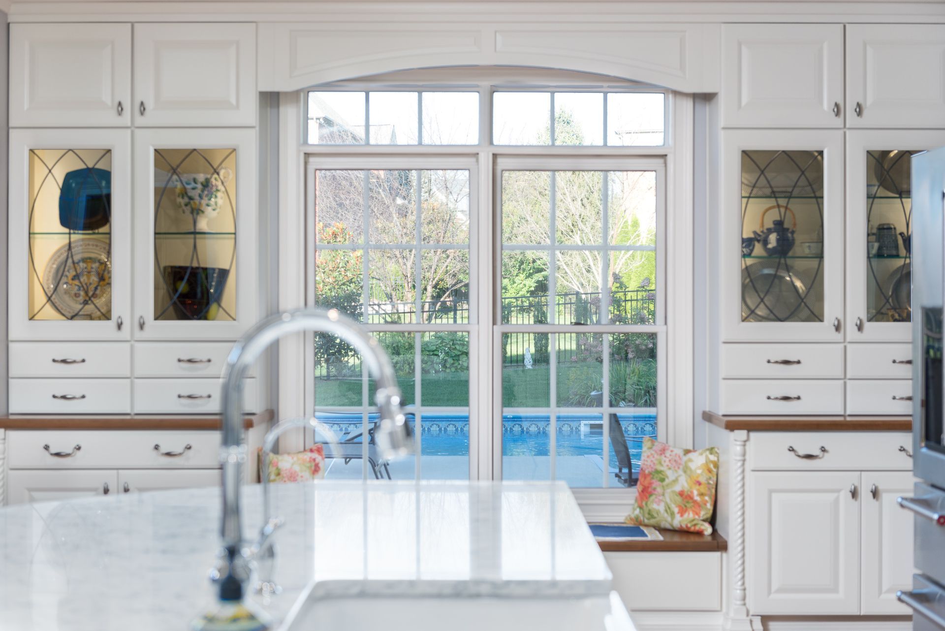 A kitchen with white cabinets , a sink , and a large window.