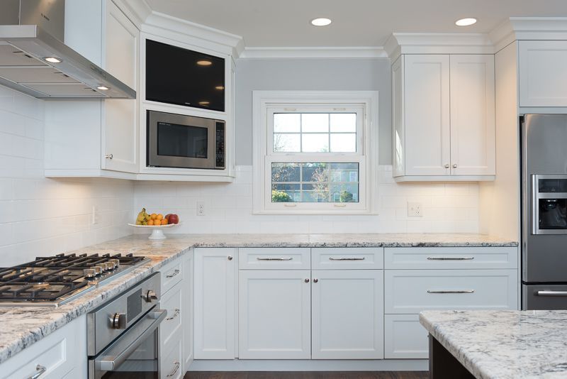 A kitchen with white cabinets , stainless steel appliances , granite counter tops and a window.