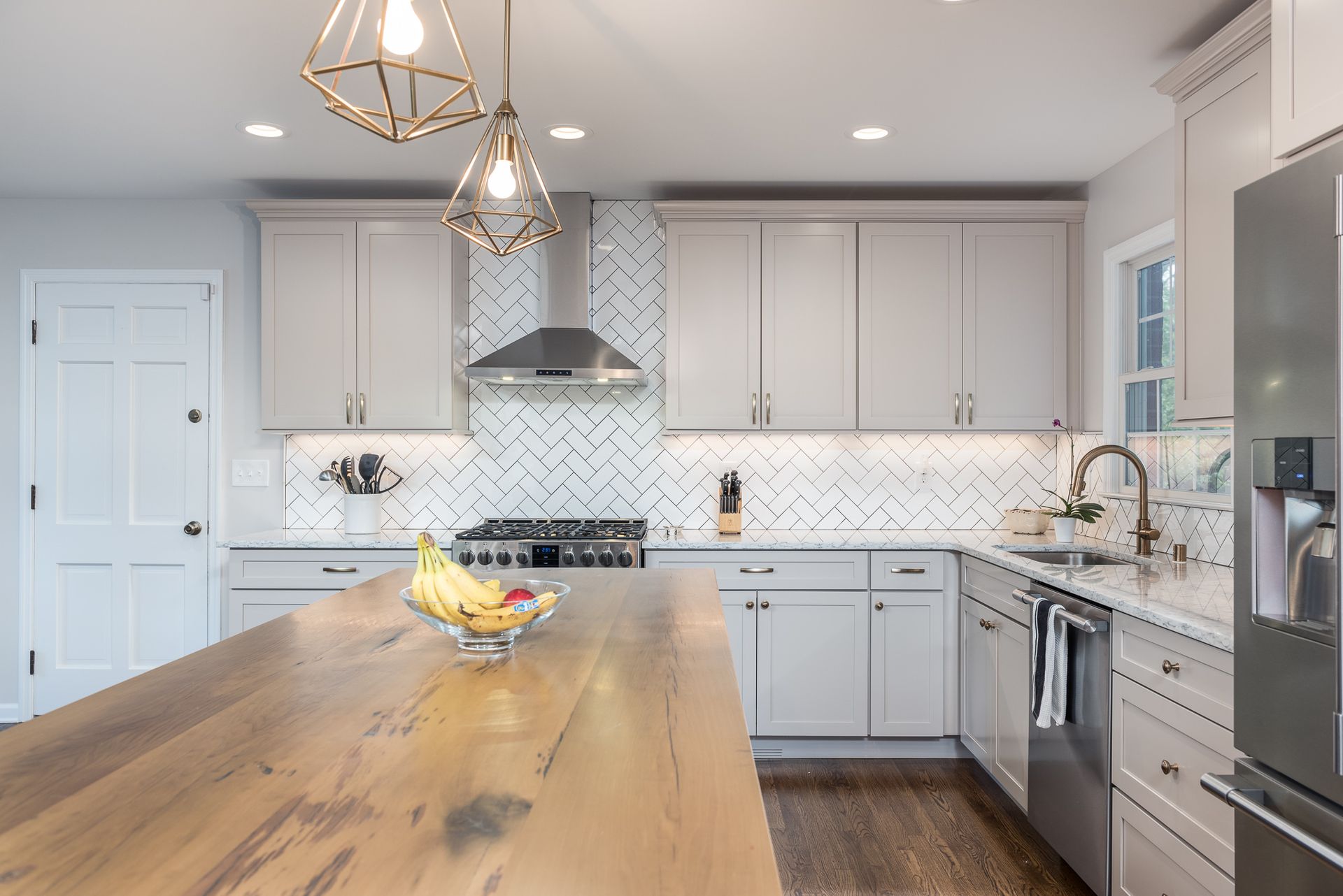 A kitchen with white cabinets , stainless steel appliances , a wooden table , and a large island.