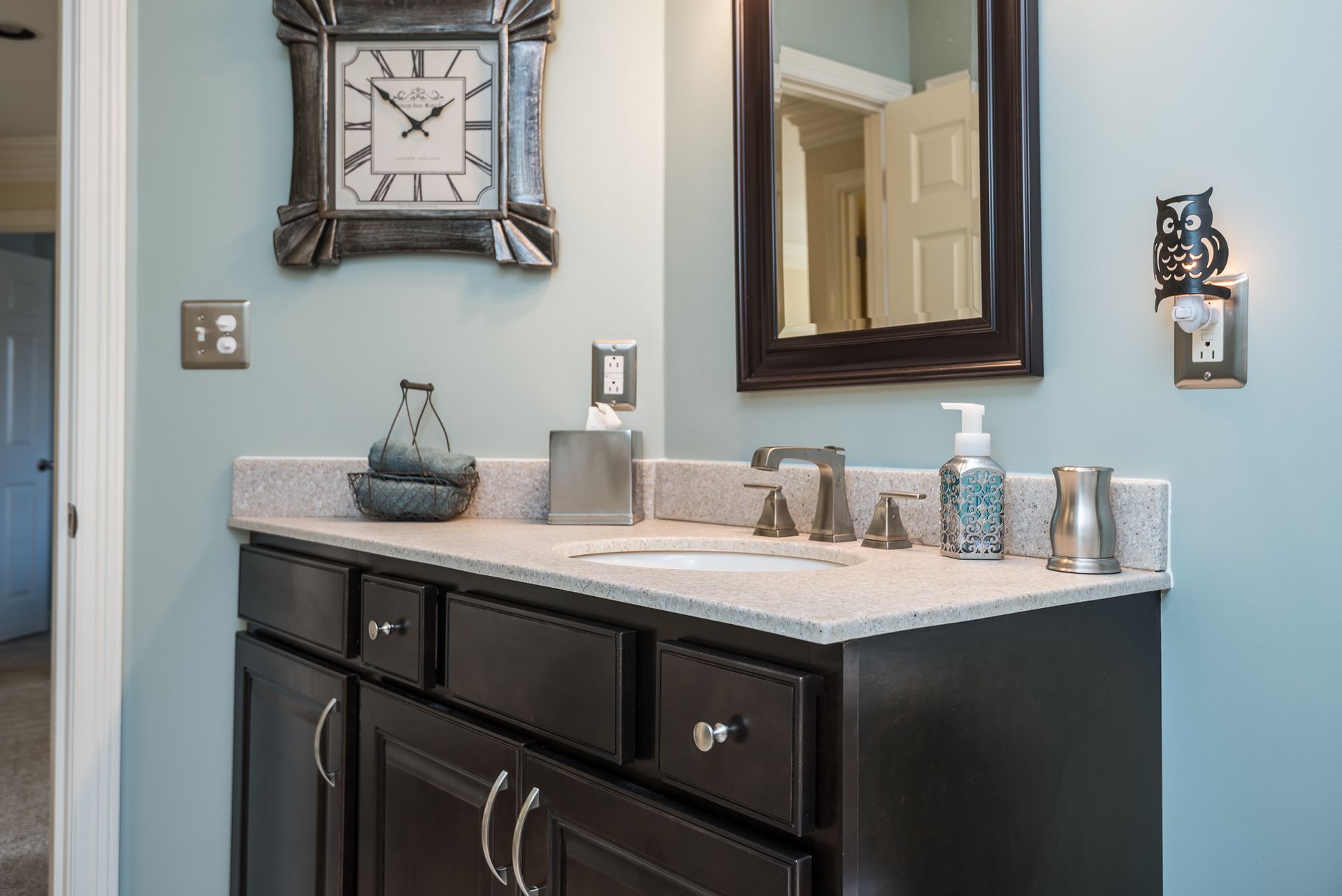 A bathroom with a sink , mirror and clock on the wall.
